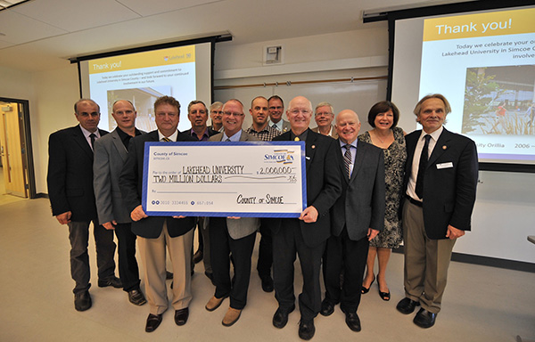 County of Simcoe Warden Gerry Marshall (centre behind cheque) presents a $2M cheque to Lakehead University President & Vice-Chancellor Dr. Brian Stevenson (holding cheque left), as Orillia Campus Principal Kim Fedderson (far right), Lakehead V.P. External Relations Deb Comuzzi, and members of County Council celebrate. 