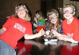 Three enthusiastic girls wearing protective eye wear showing of their dissected frog