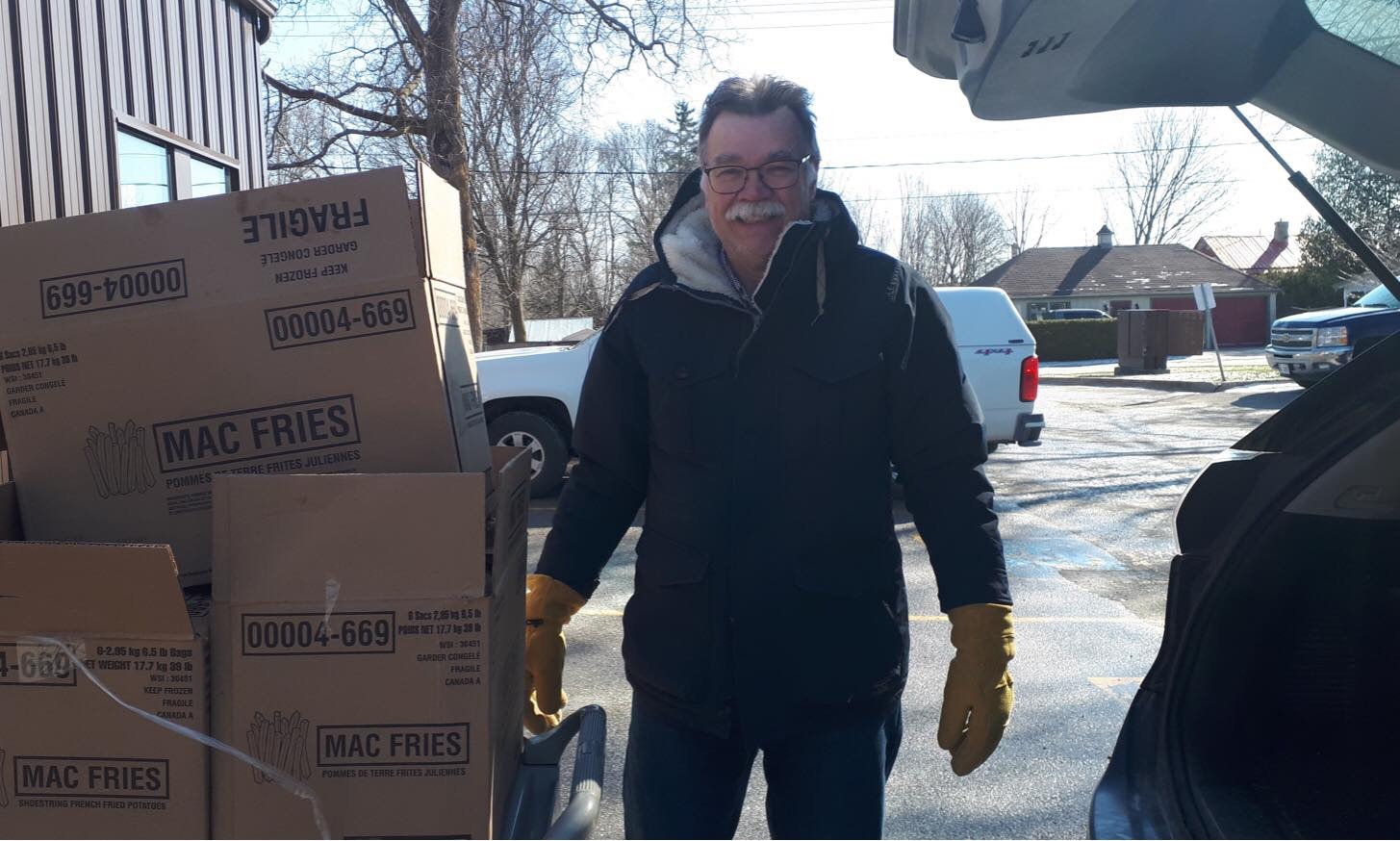 Mike Taylor wearing a winter coat standing outside beside a stack of boxes
