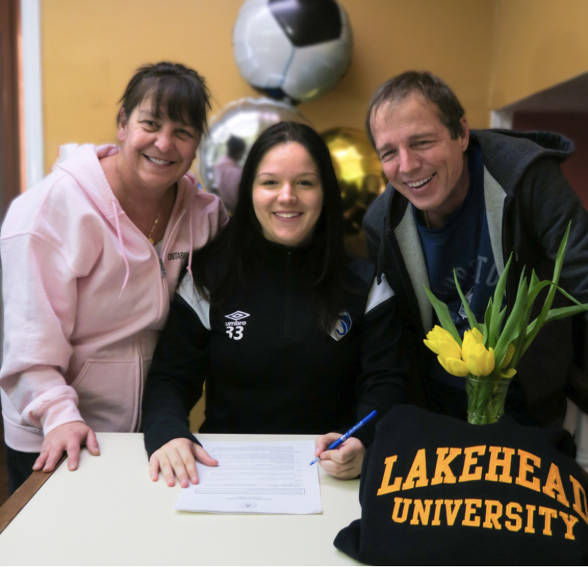Abbygayle Welch sits a table with a pen, with her parents on either side of her, and prepares to sign her Lakehead soccer contract