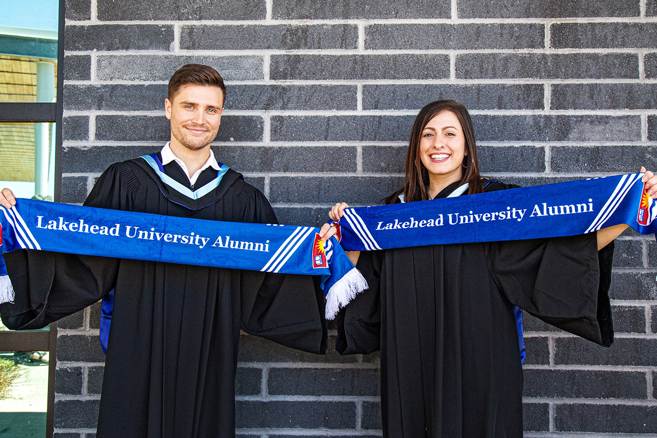 Two graduating students holding Lakehead alumni scarves