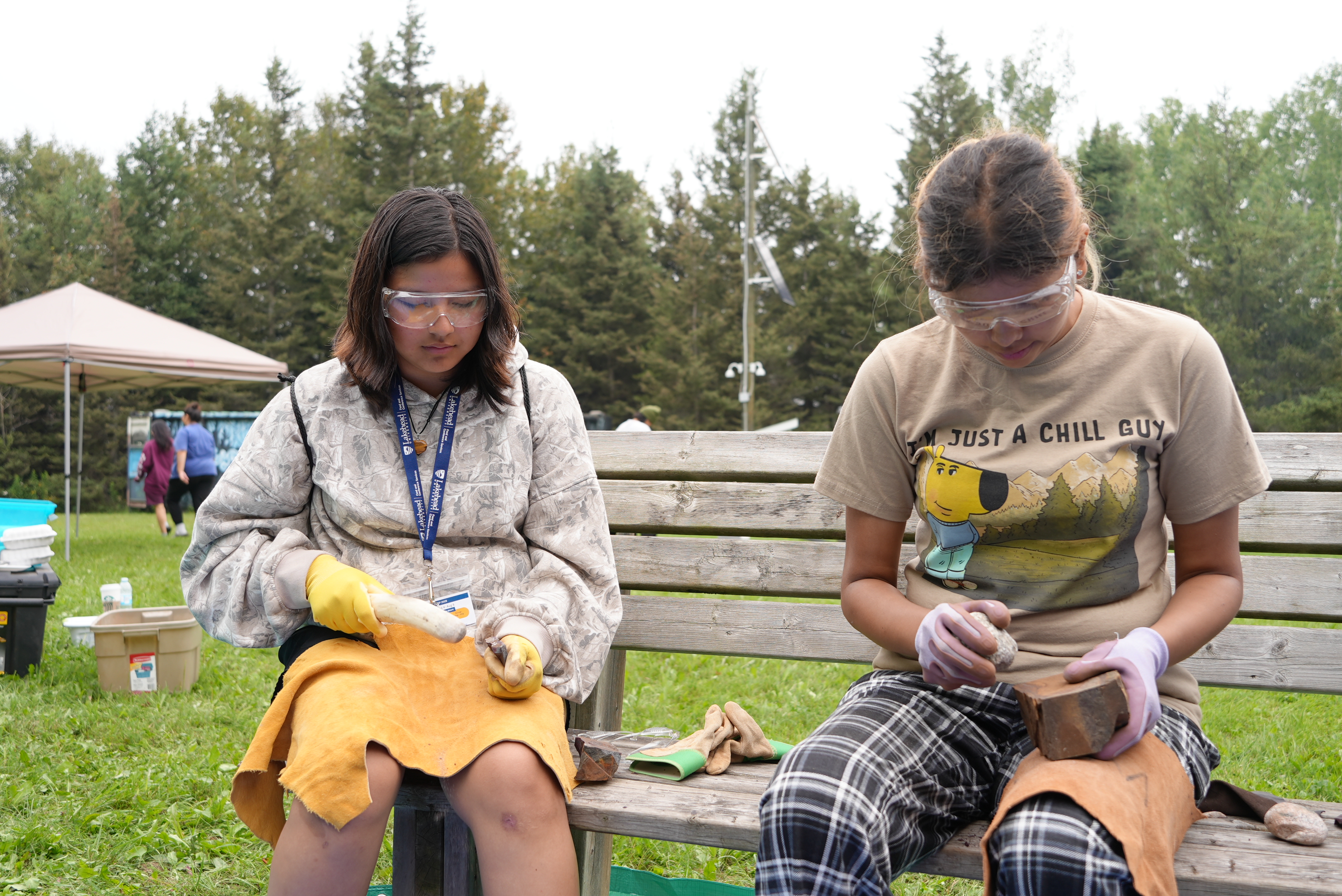 Two Outland students sit on a bench doing flintnapping as part of experimental archaeology programming