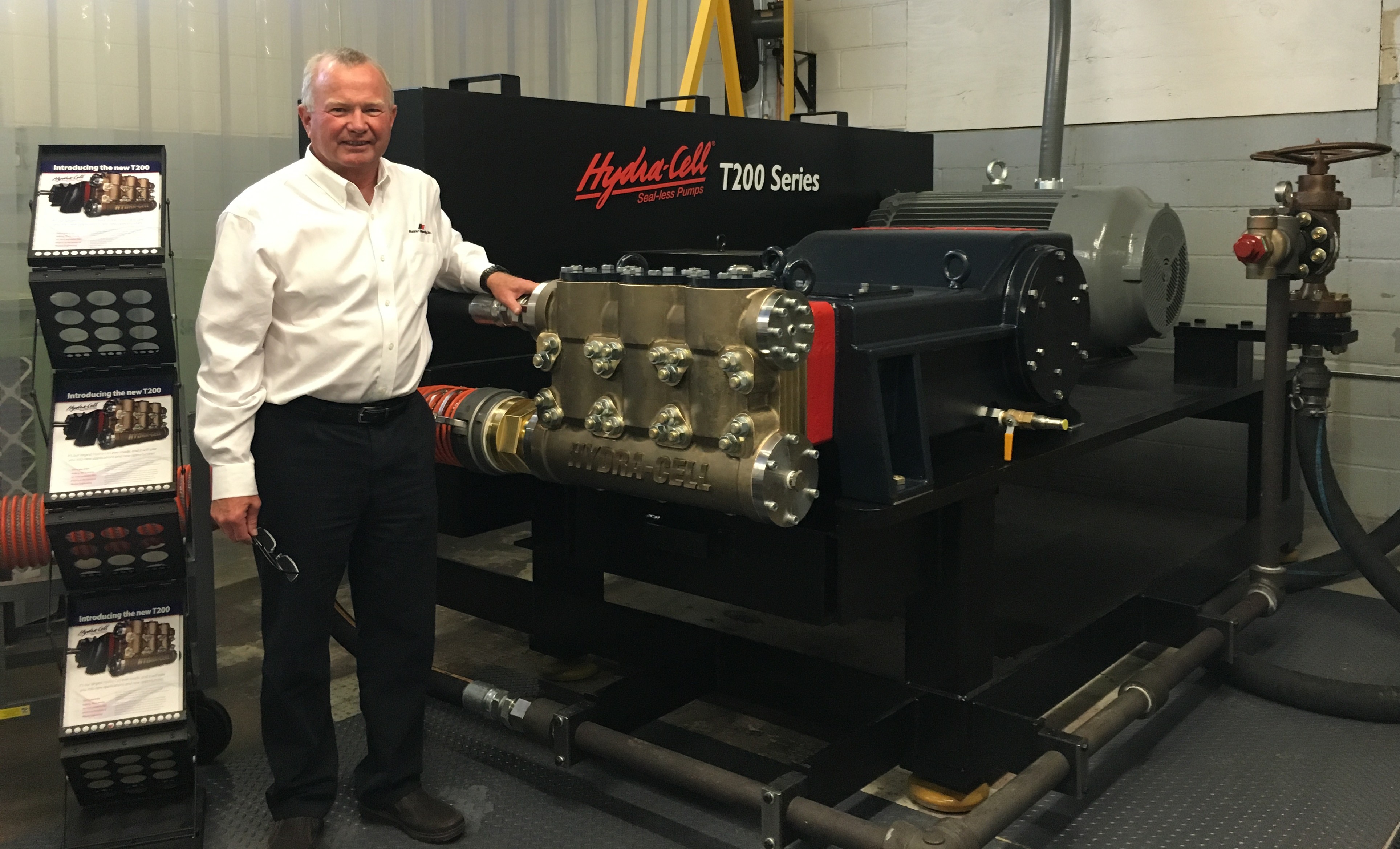 Dick Hembree stands in an industrial facility beside a Hydra-Cell T200 Series pump