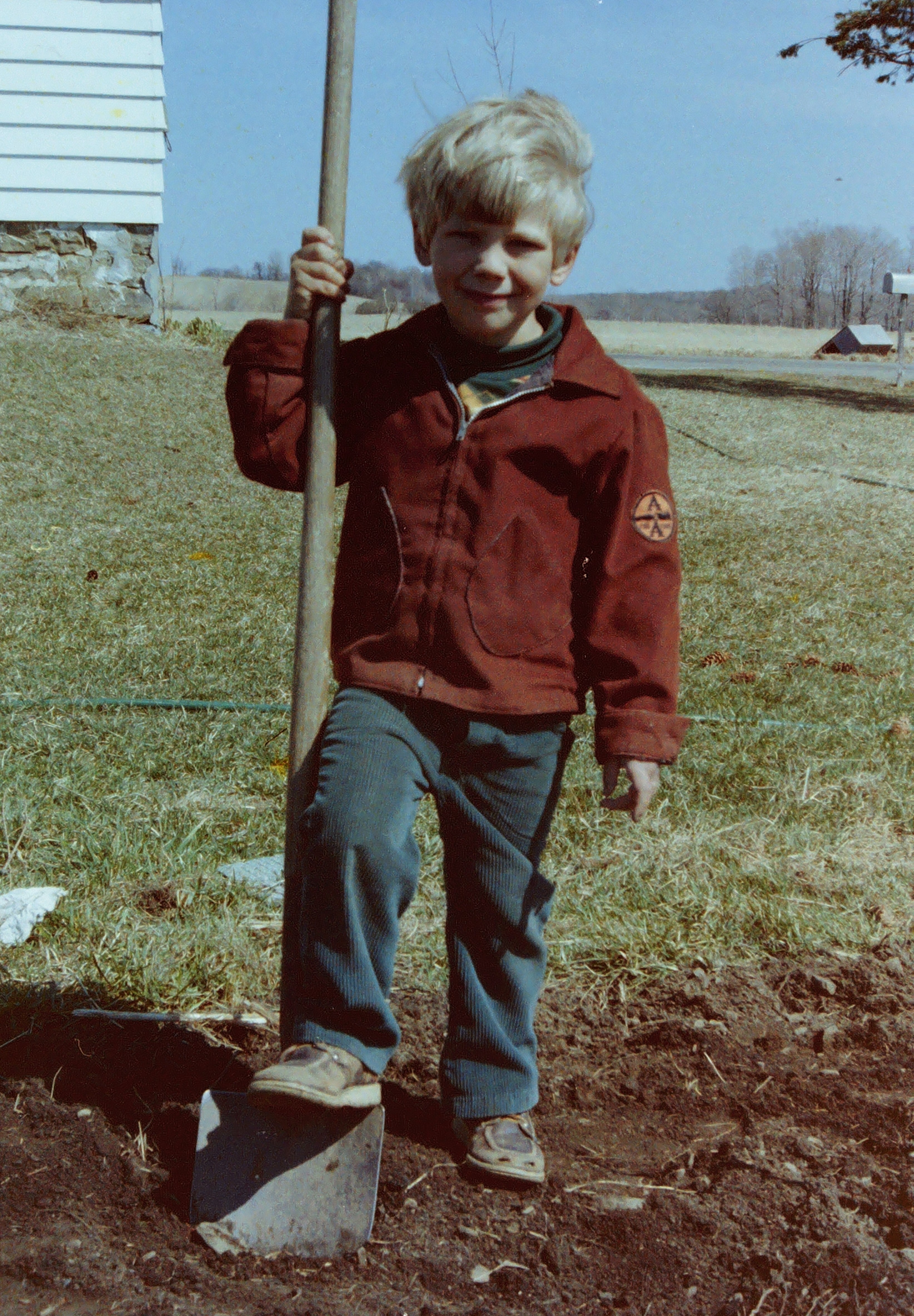 Five-Year-Old Nathan Basiliko stands with his foot on a shovel on a patch of dirt on his family farm
