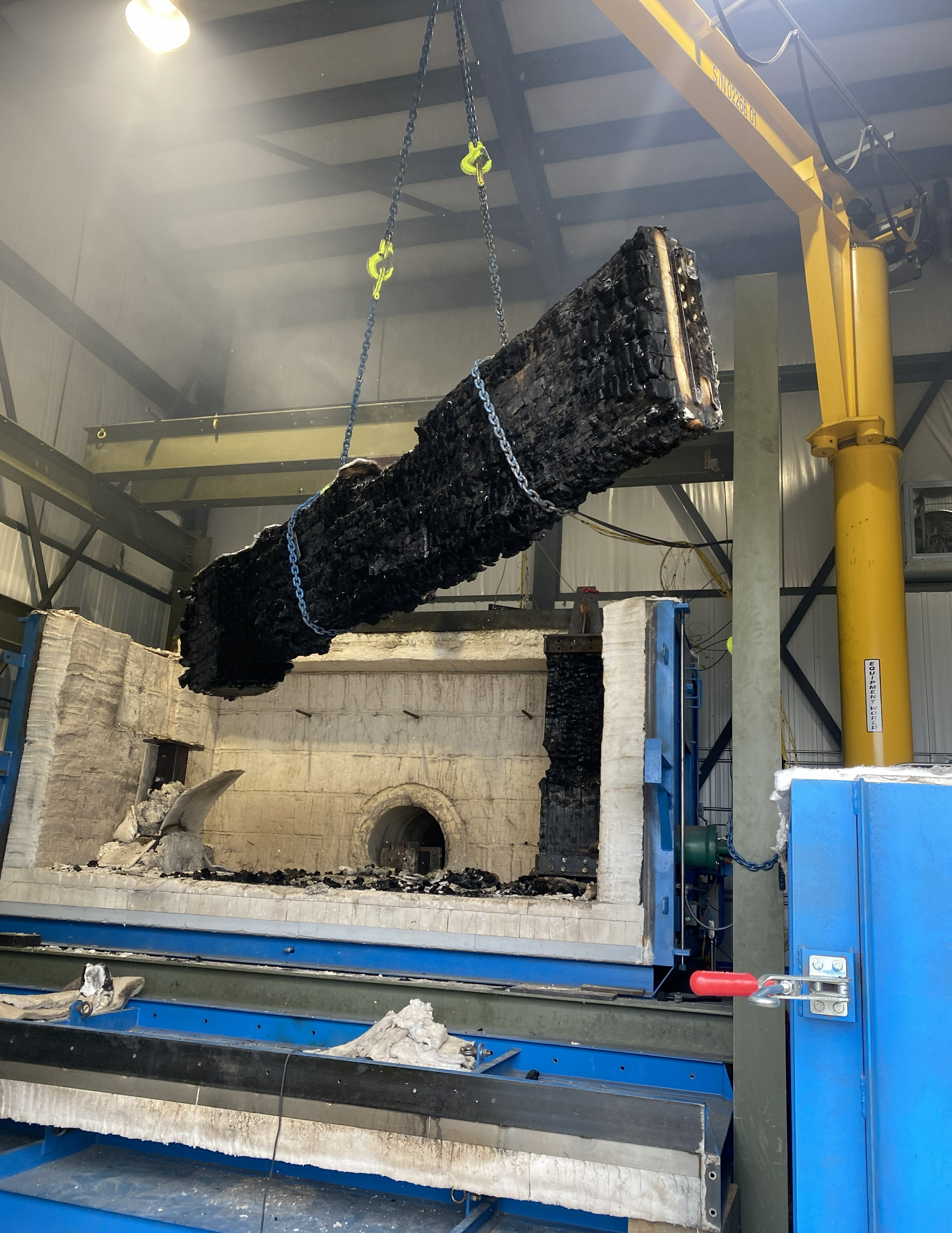 A charred beam is removed from a fire-testing furnace using a crane