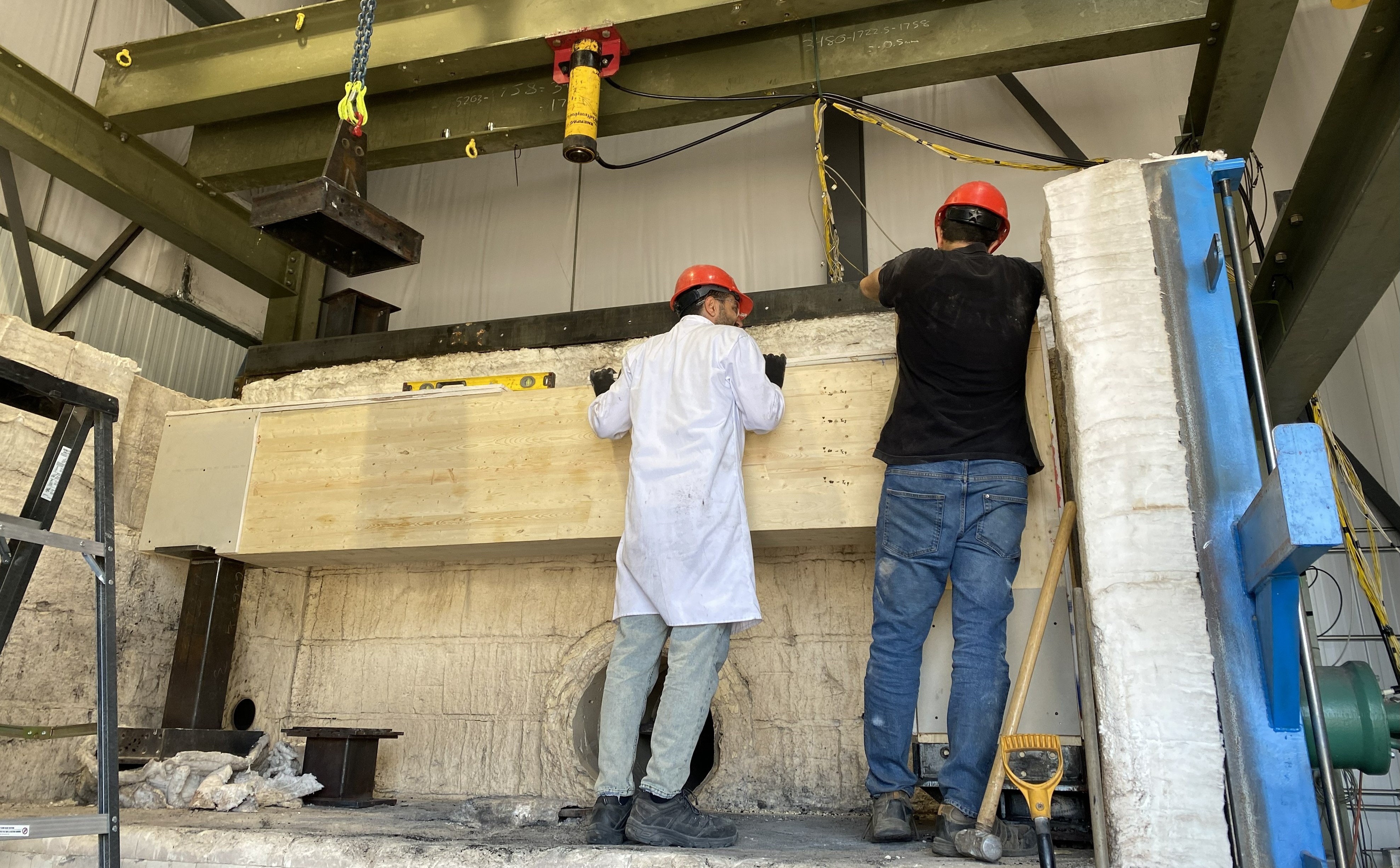 Setting Up a Fire Test Two members of Dr. Sam Salem's research team, wearing hard hats, set up a fire test in Lakehead's Structural Fire Testing & Research Laboratory