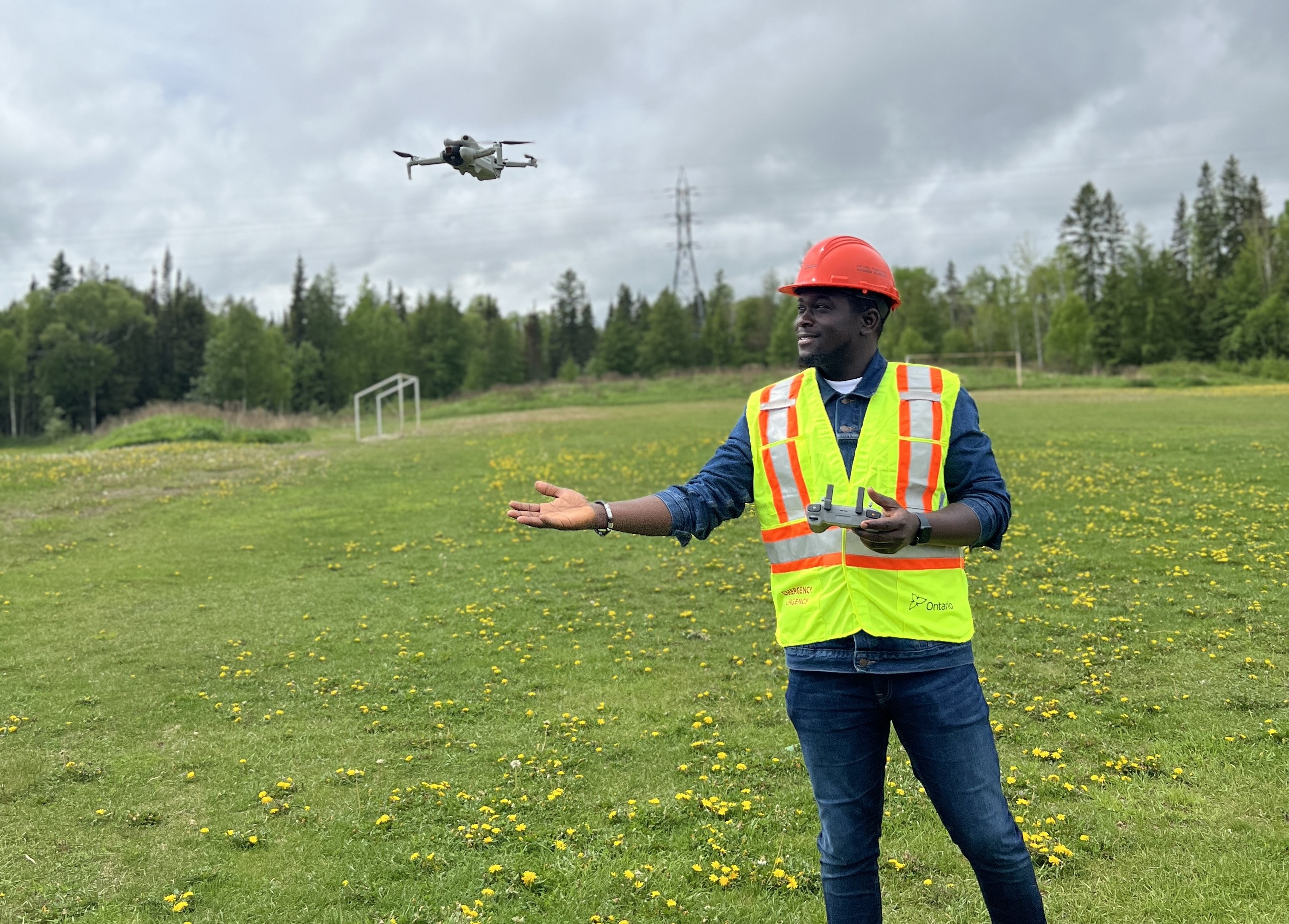 Temitope Ojo, wearing a hard hat and safety vest, flies a drone in a field