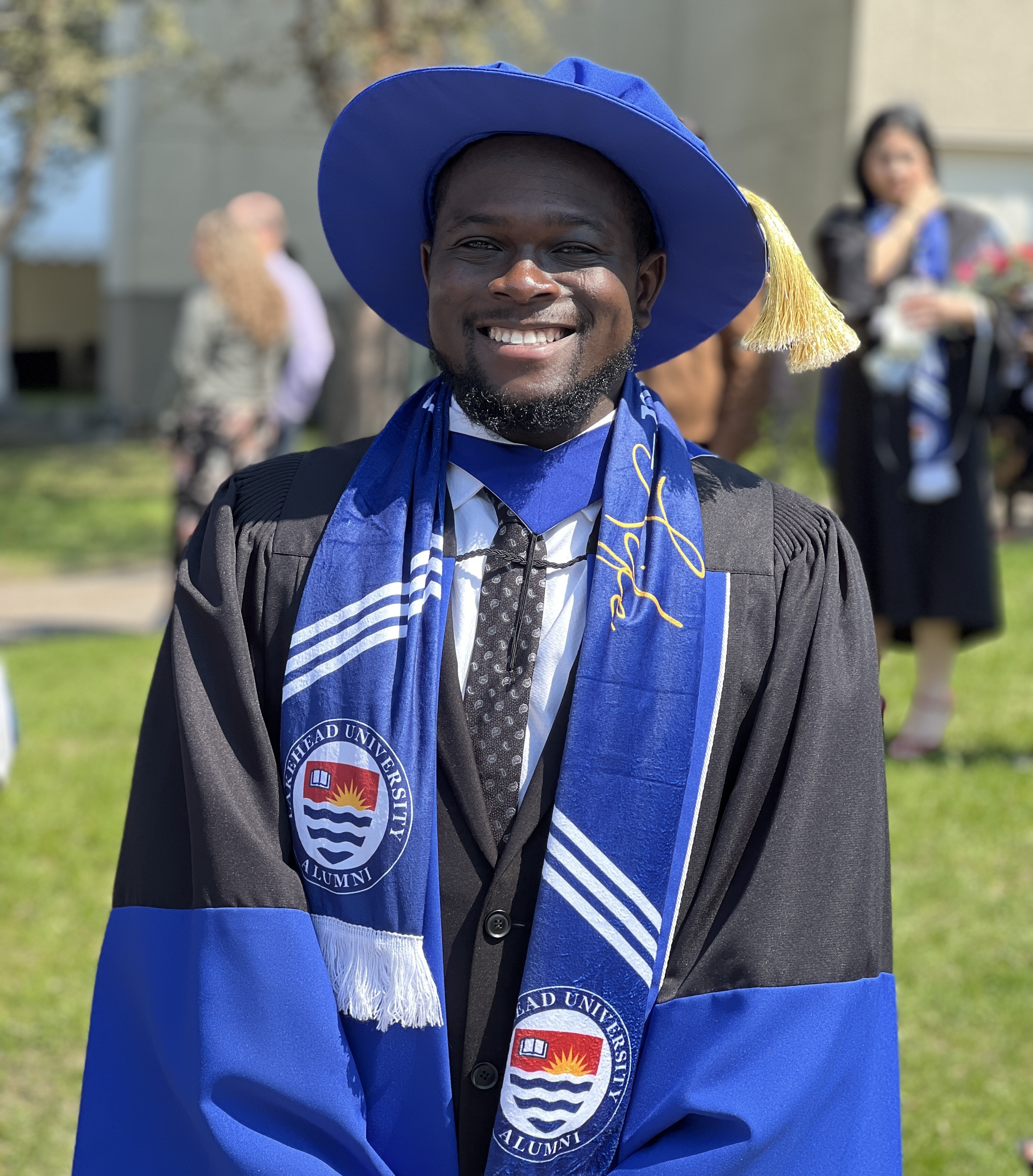 Dr. Temitope Ojo, wearing convocation robes, stands outside the Thunder Bay Community Auditorium after receiving his PhD in 2024