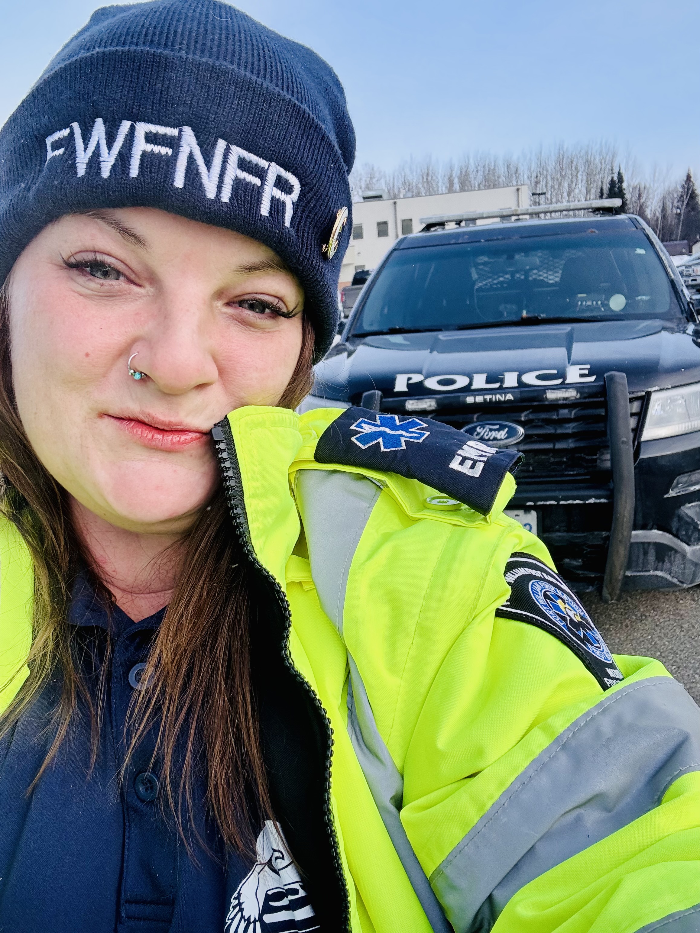 Erin Christiansen, wearing an EMR work jacket, stands in front of a police car on Fort William First Nation