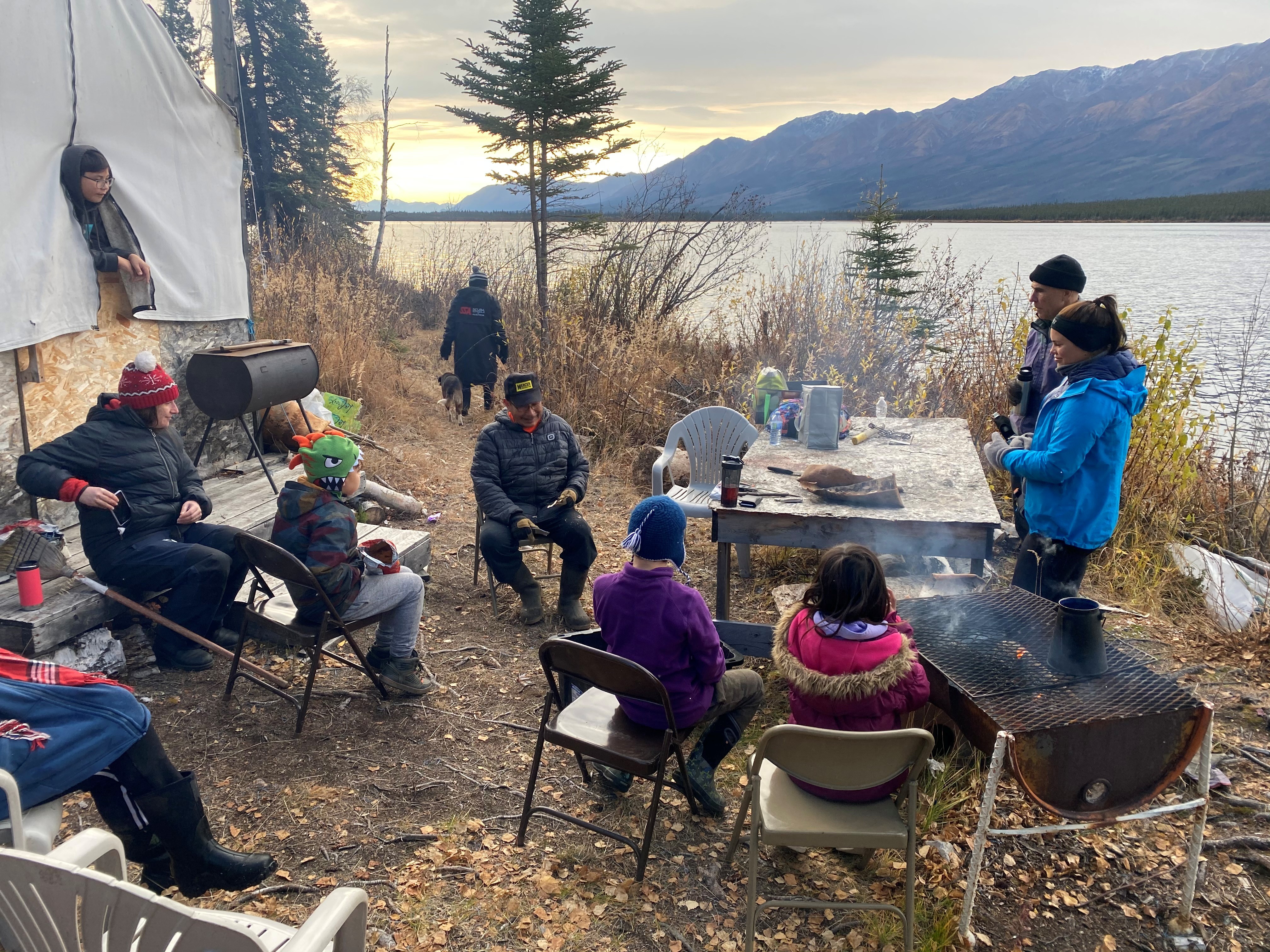 Elementary school students and chaperones sit at the edge of a lake with a mountain on the far shore