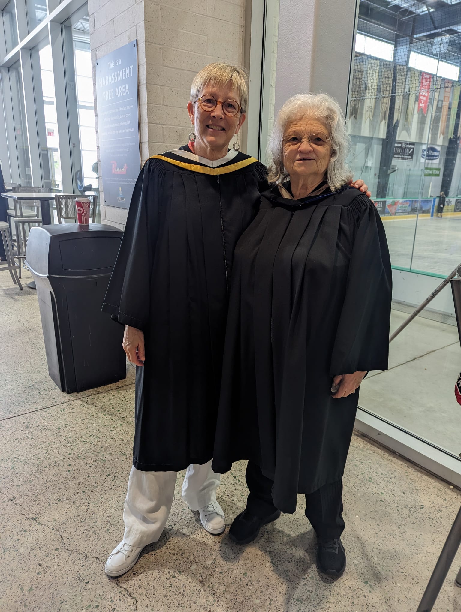 Holly Gray and Ginny Majury stand next to each other wearing convocation robes