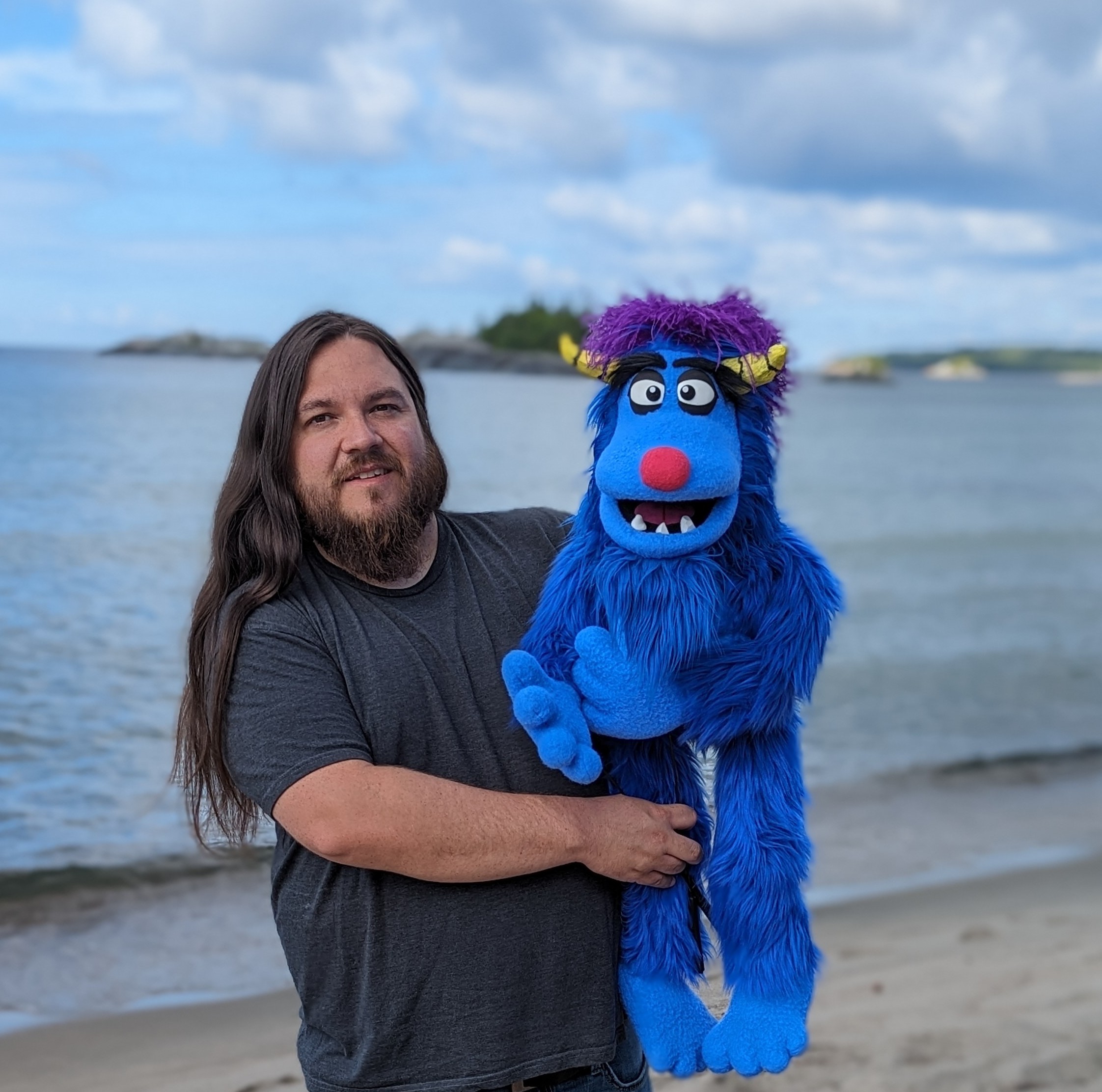 John-Paul Chalykoff stands on a beach holding his puppet Baabii