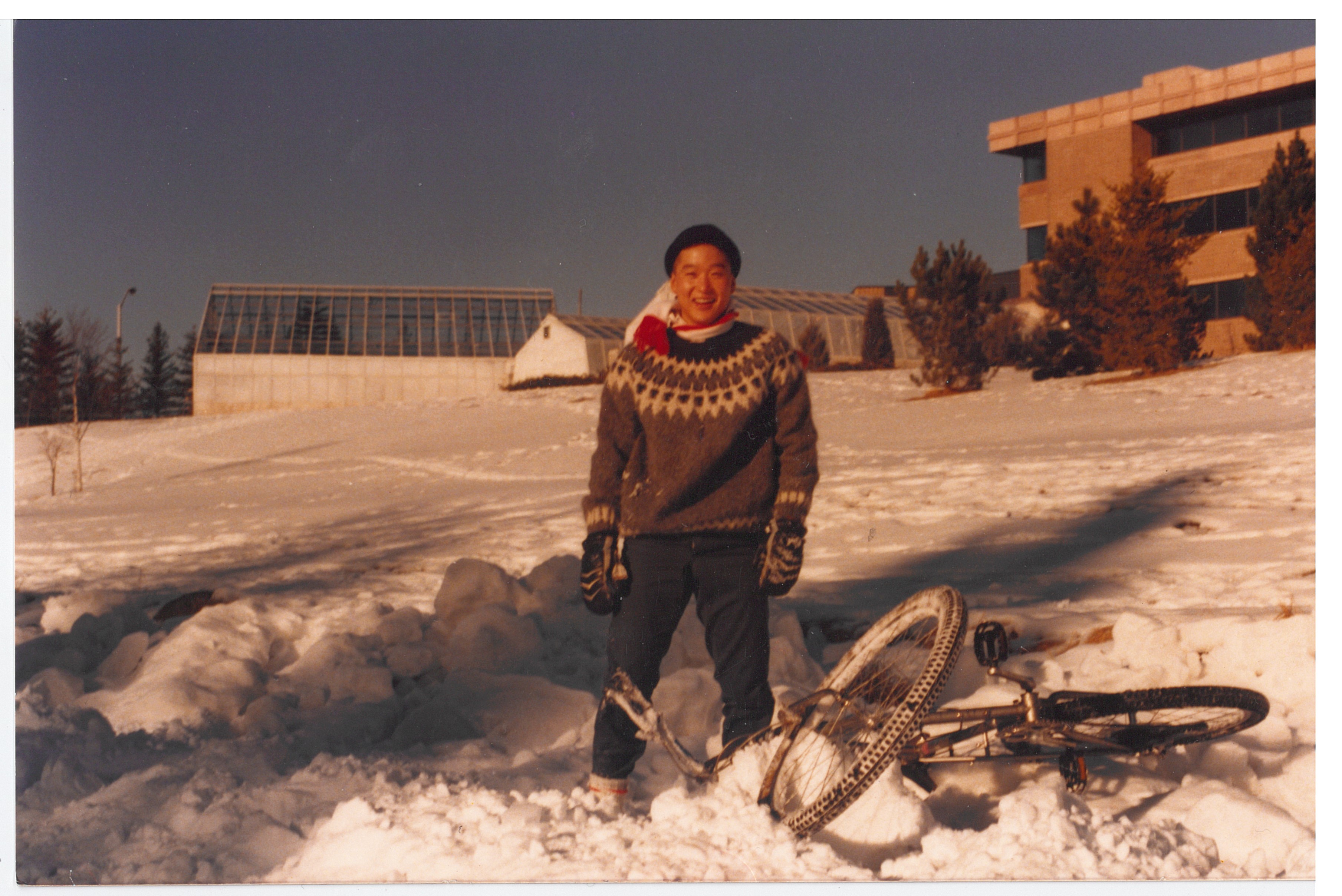 Forestry student Dave Kim wearing a knitted winter cap and sweater stands beside his mountain bike by Lake Tamblyn in 1986
