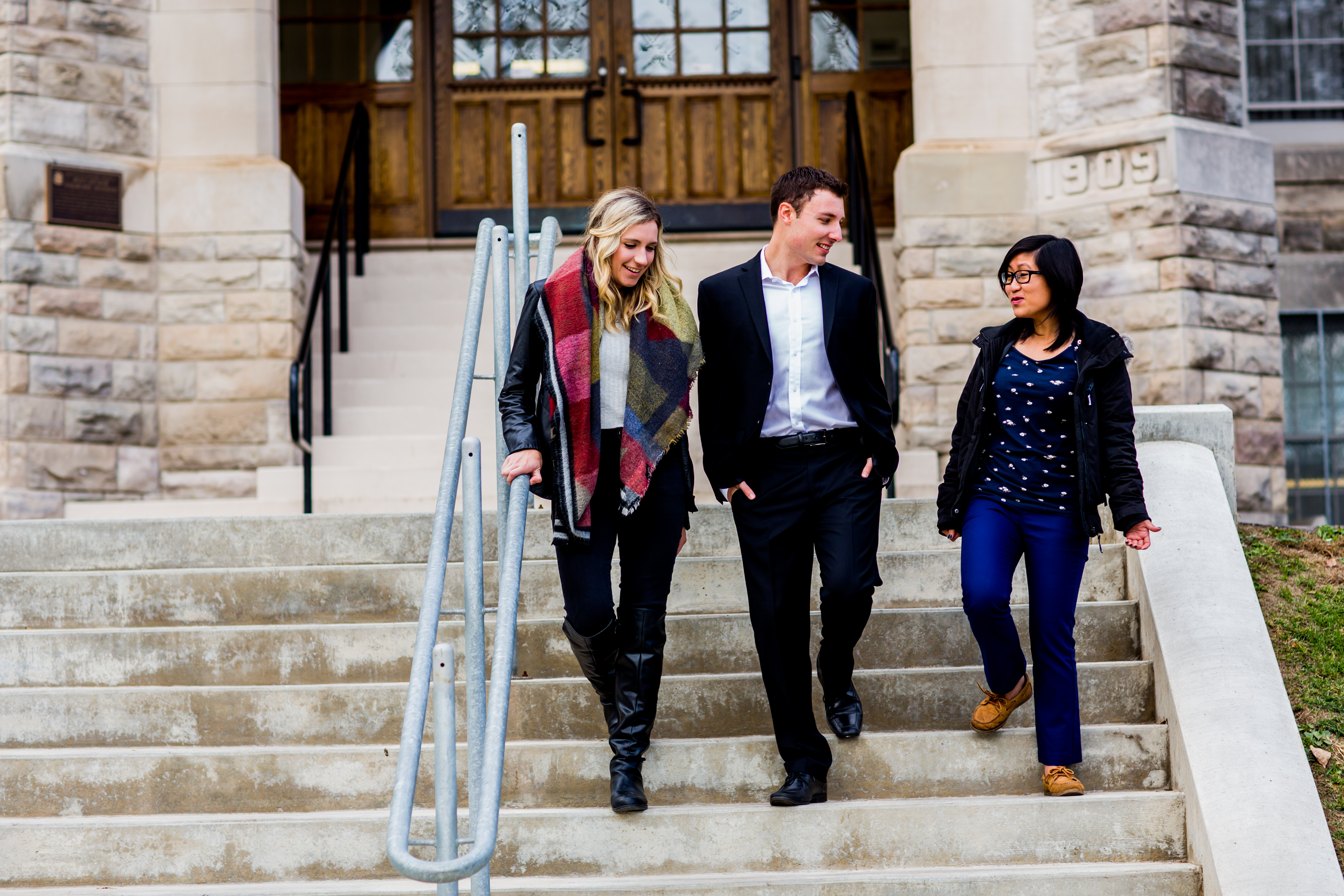 Three Lakehead law students talk to each other as they walk down the steps at the entrance of the PACI Building