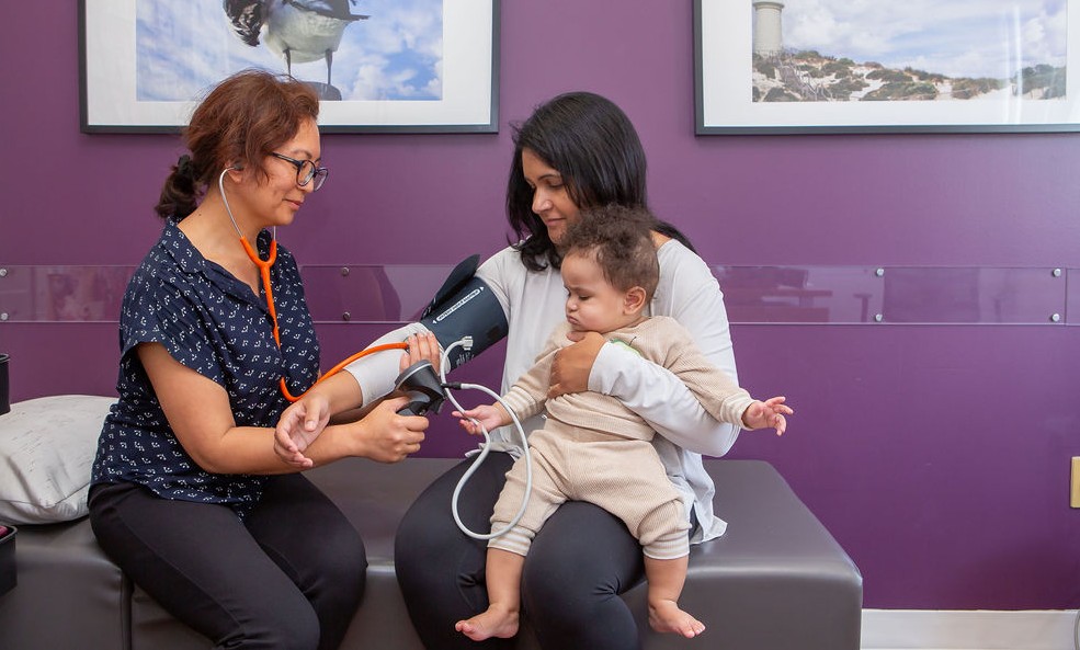 A midwife takes the blood pressure of a mother holding a baby