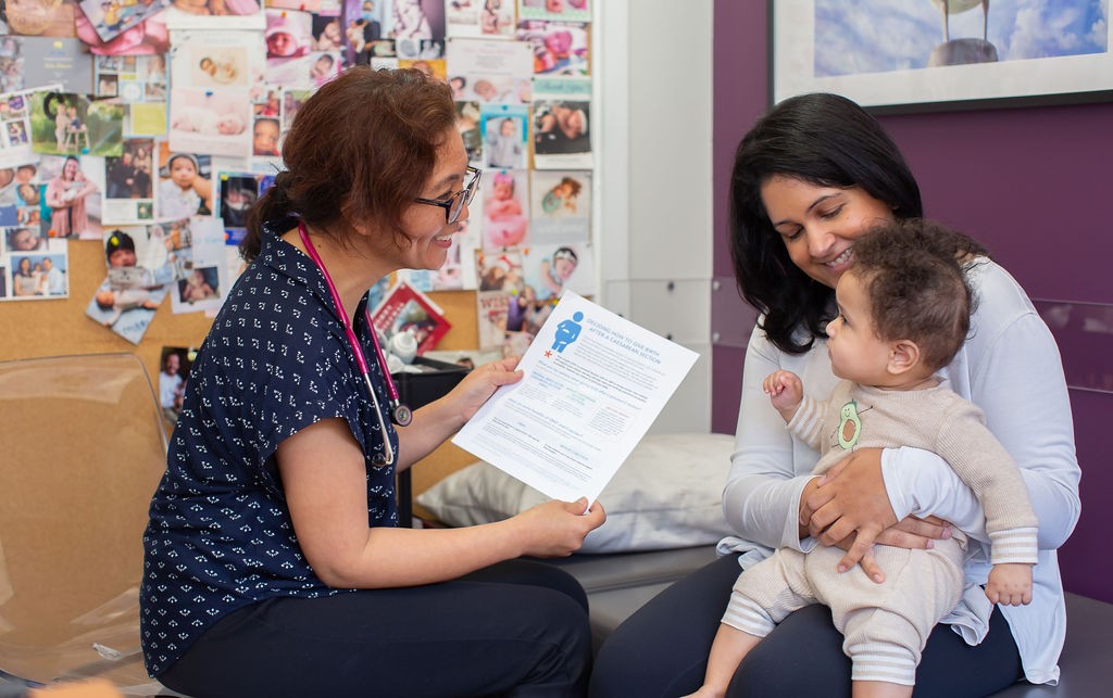 A midwife shares an information sheet with a mother holding a baby