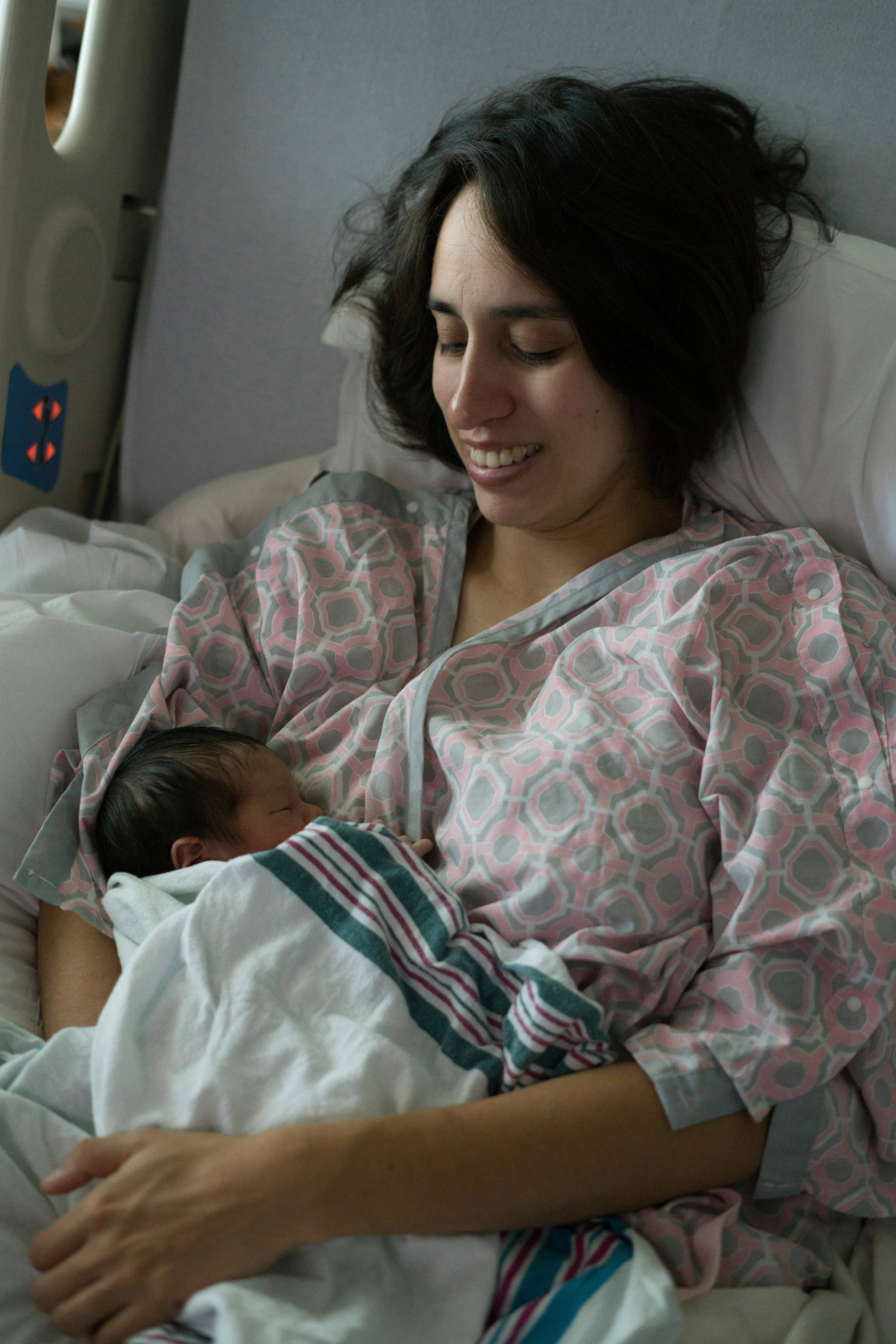 A woman seated upright in a hospital bed holds her newborn baby
