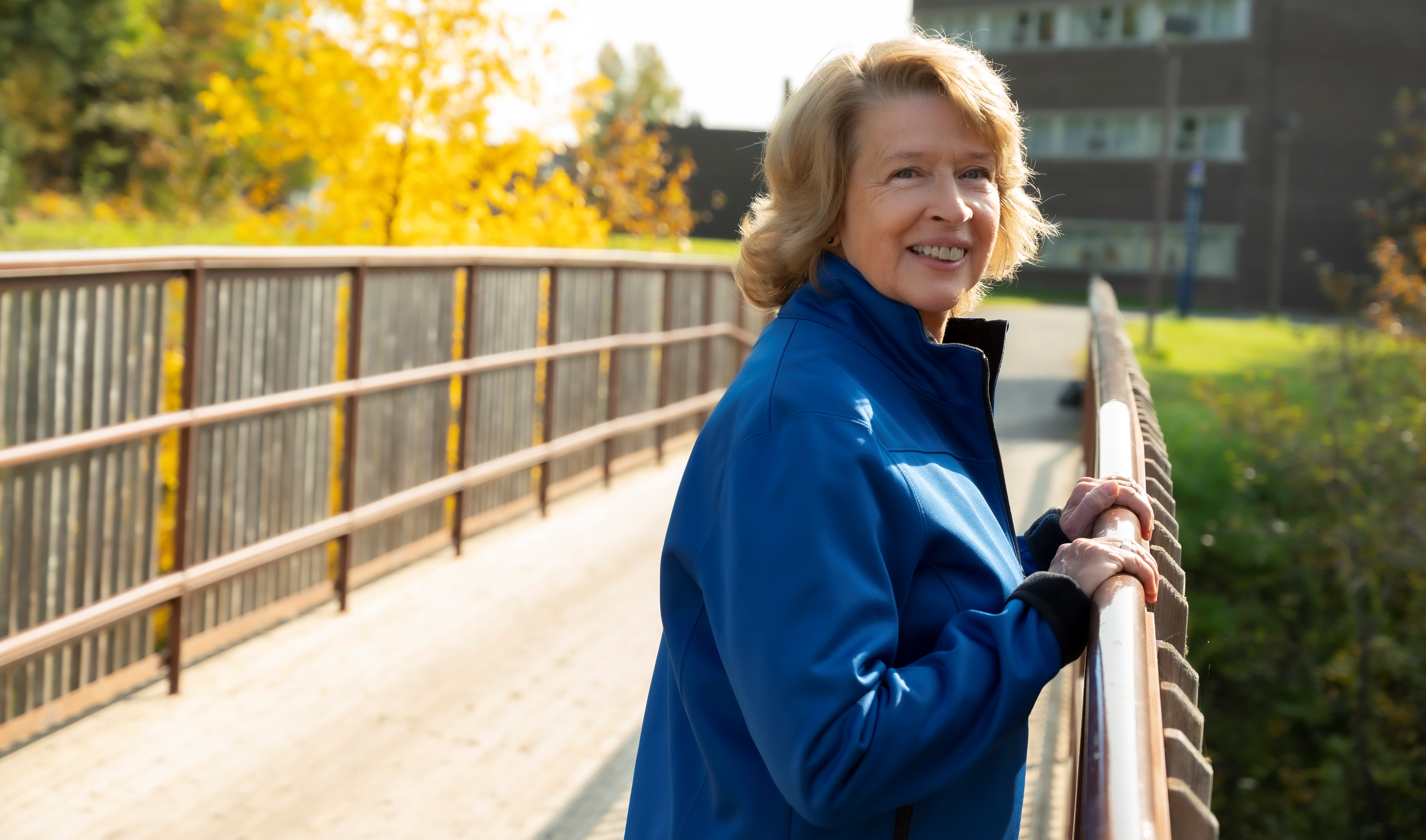 Lakehead President Moira McPherson leans against a bridge on the Thunder Bay campus
