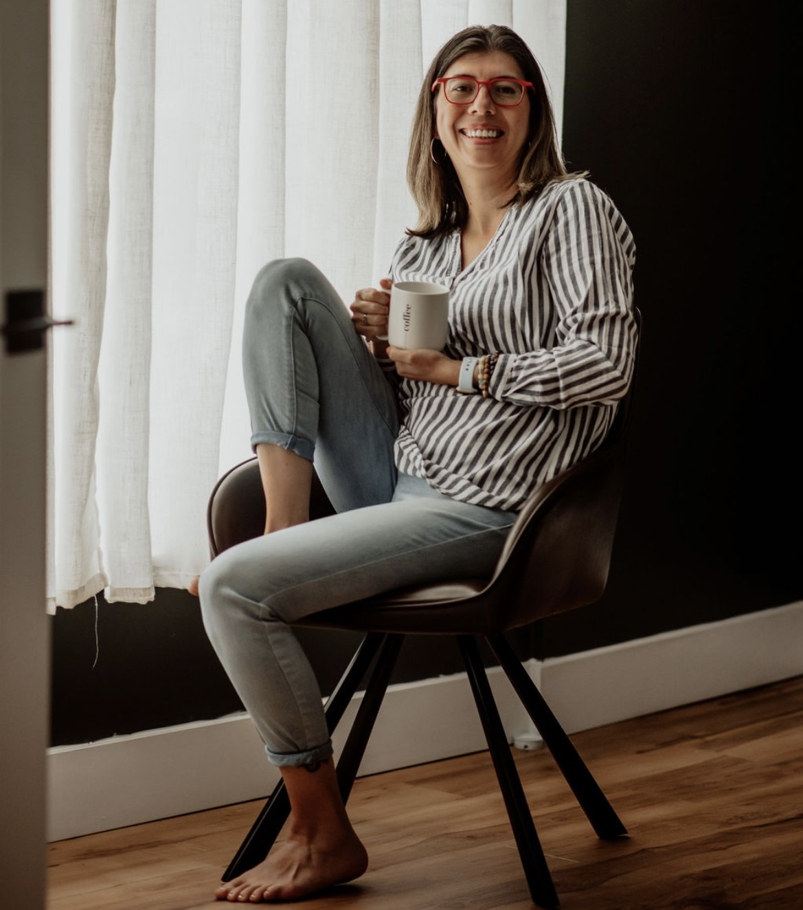 Sandy Falcon sits in a chair while holding a coffee mug