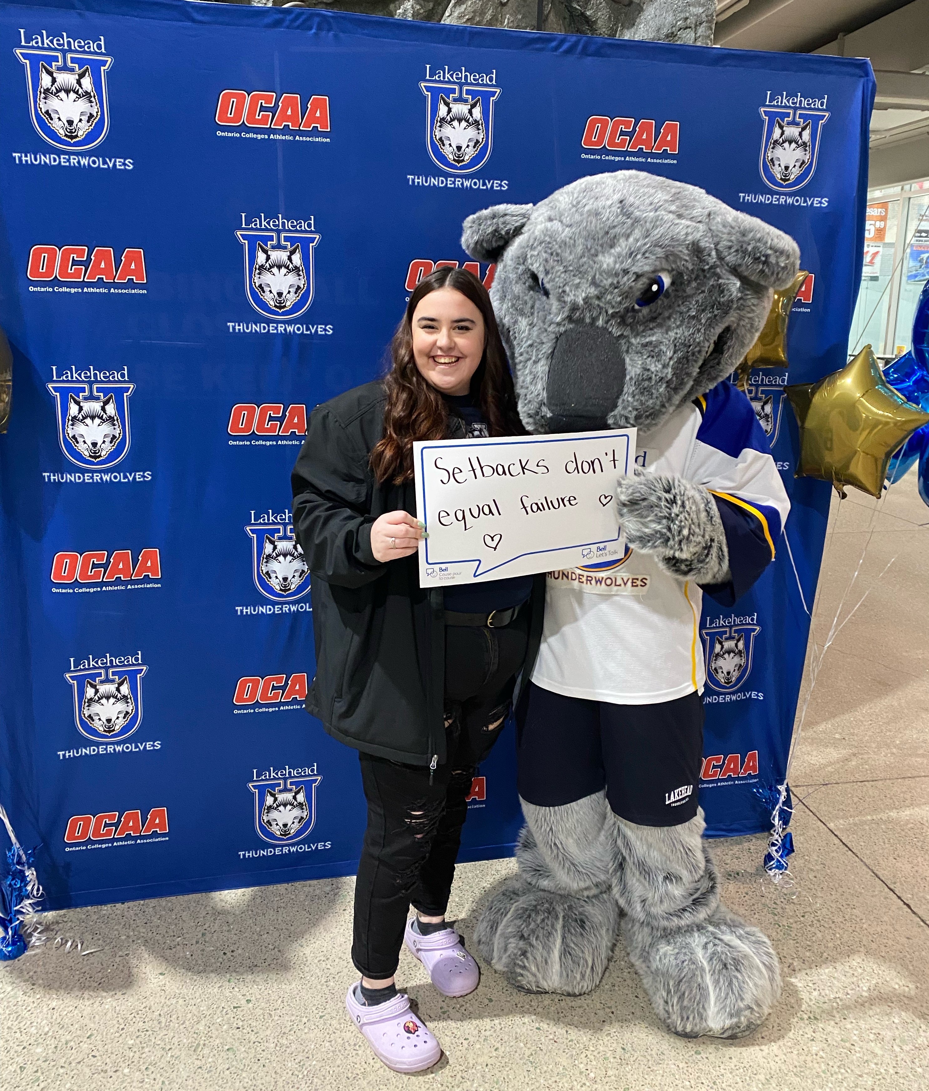 Taliah Lalande stands with the Thunderwolves Wolfie mascot holding a sign saying "Setbacks don't equal failure"