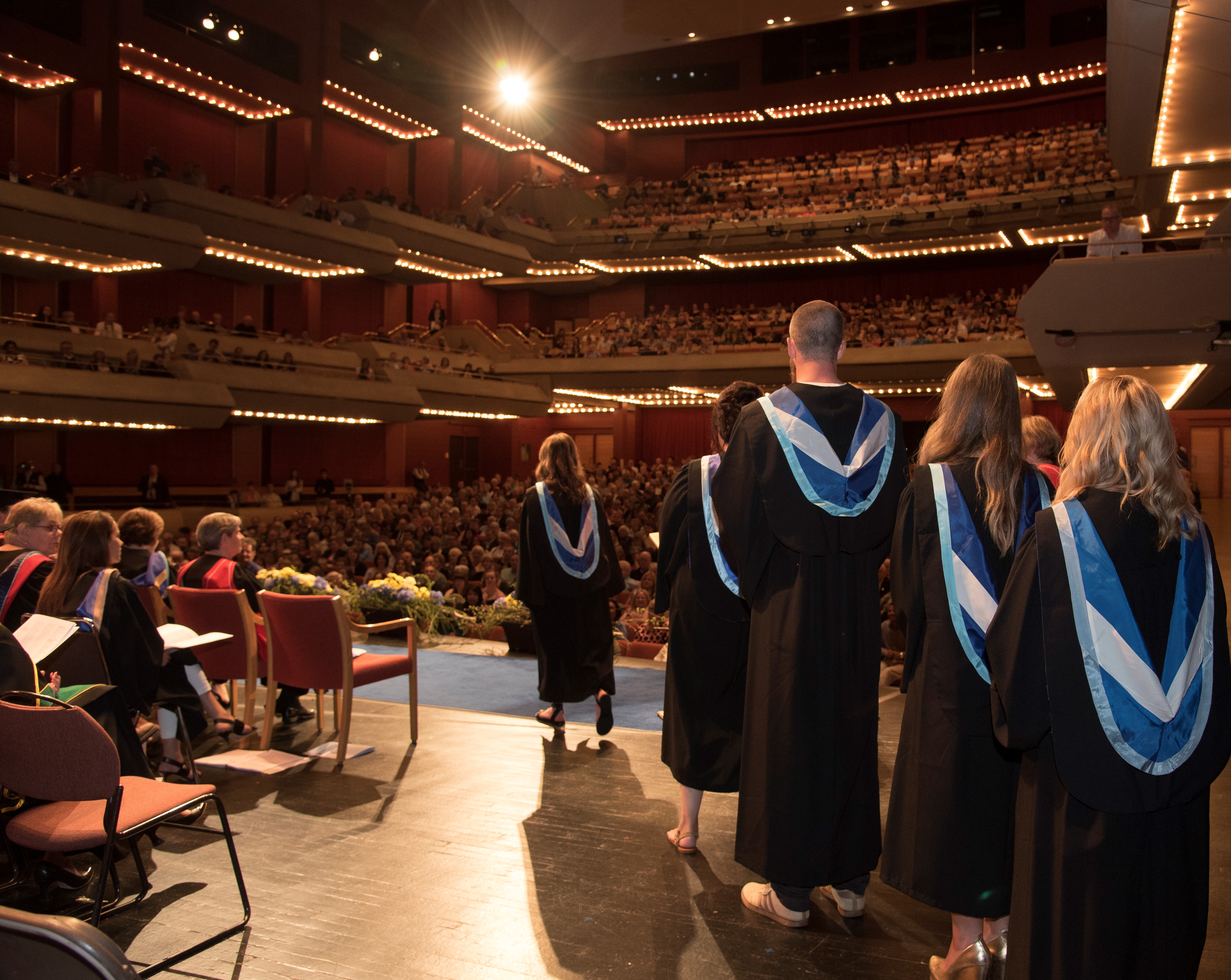Back view of Lakehead students in robes walking across stage to receive diplomas
