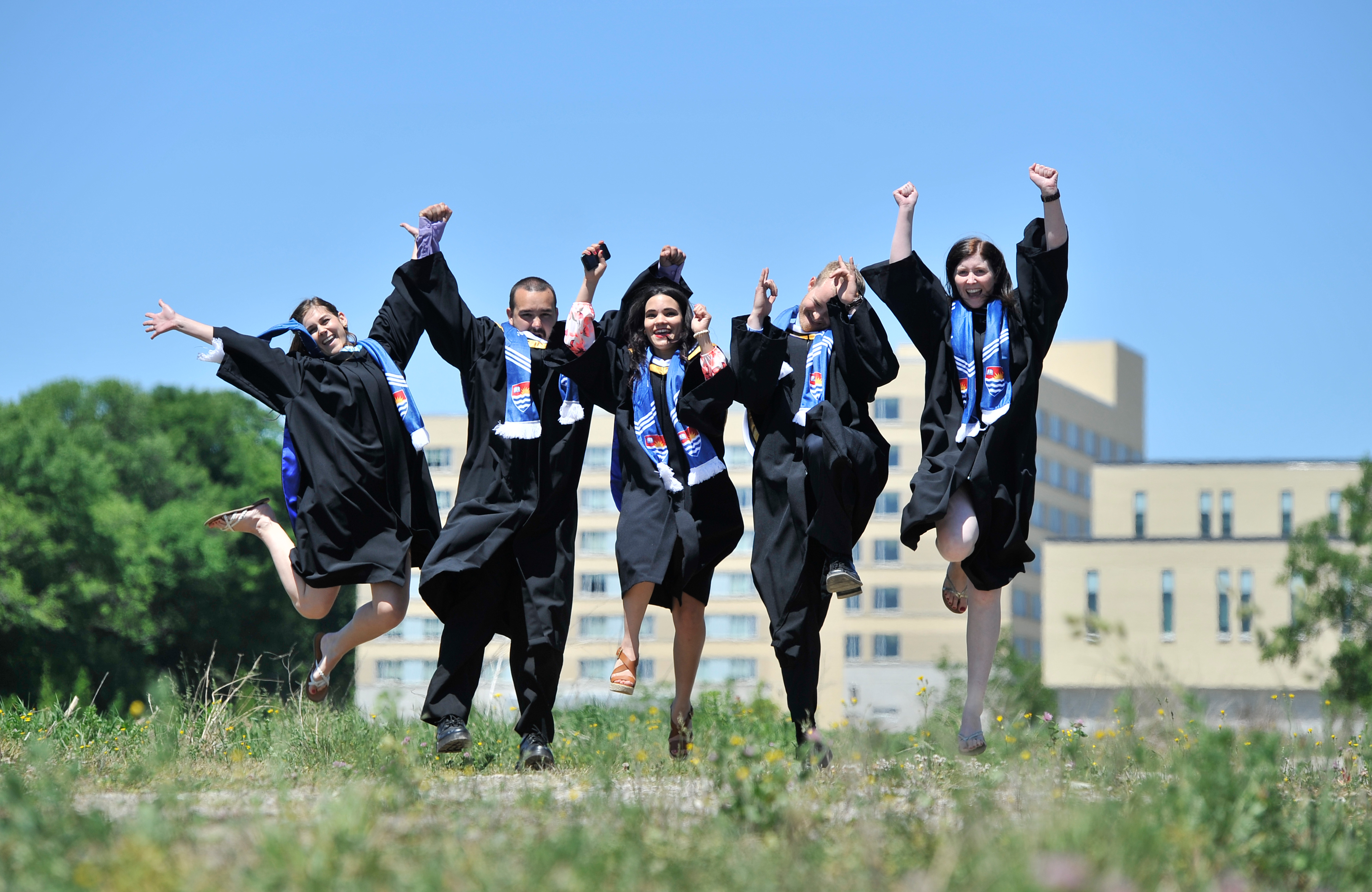 Four Lakehead Orillia students wearing convocation robes jump in the air