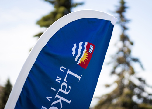 A flag featuring the Lakehead University logo over a backdrop of beautiful trees