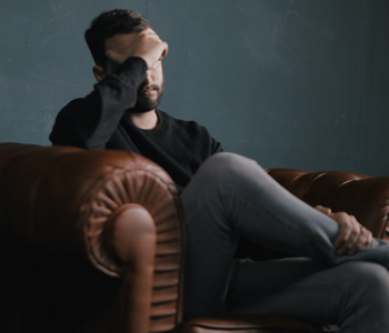 A man sitting in a large leather chair clearly stressed with his hand on his face