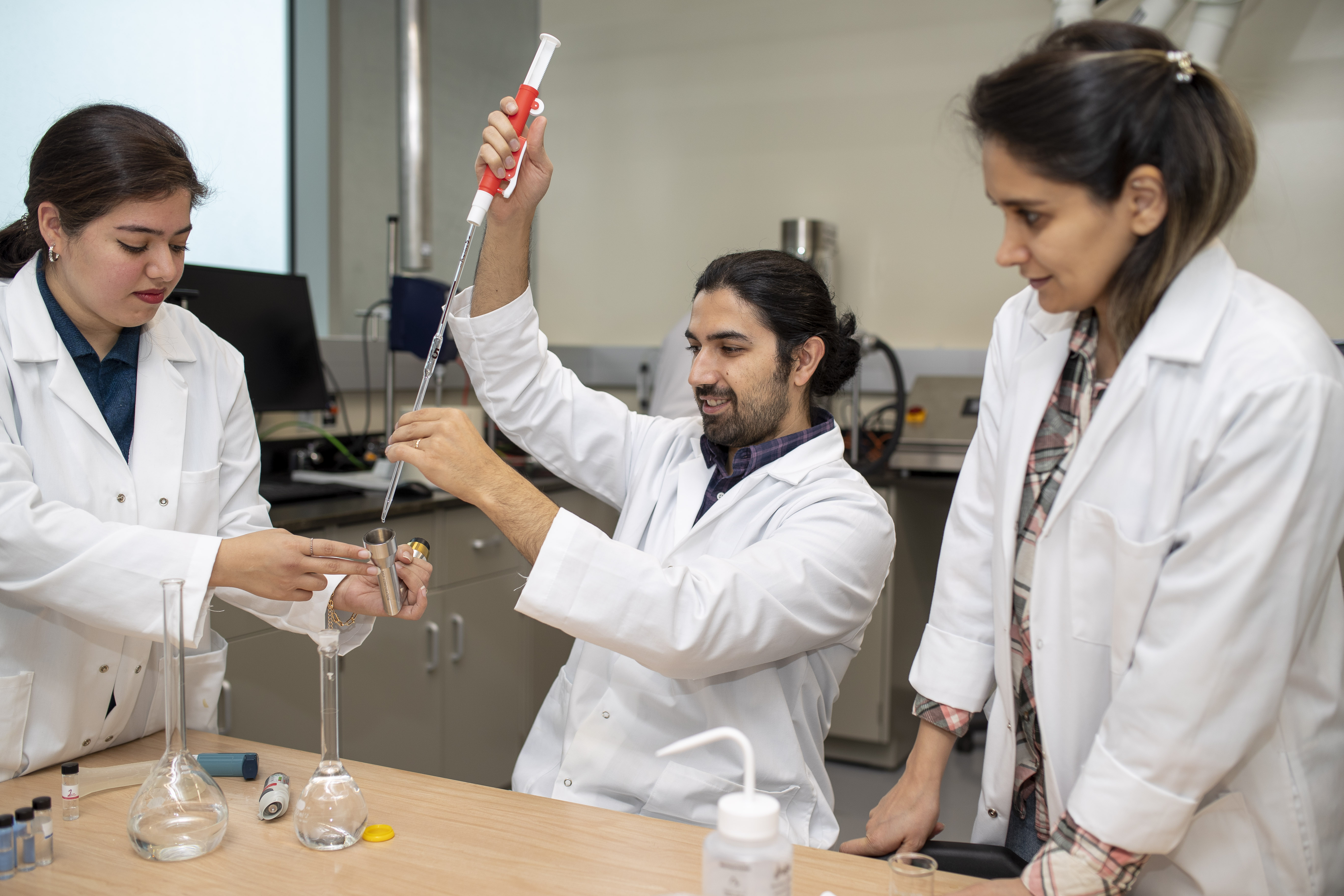 Three graduate students using equipment in chemical lab