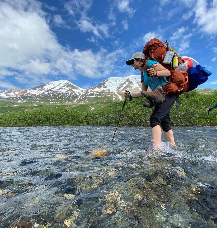 Emmalee crossing a river with a fully loaded backpack