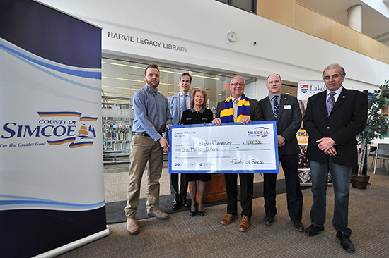 Lakehead Orillia student Cody Avery, Lakehead Orillia Principal Dr. Dean Jobin-Bevans, Lakehead Interim President and Vice-Chancellor Moira McPherson, Warden Gerry Marshall, Mayor Basil Clarke, and Mayor Mike Burkett are pictured holding a cheque for $1-million