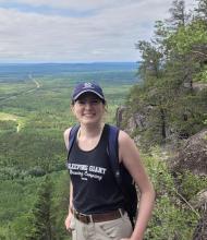 Paige stands on a cliff overlooking the woodlands around Nipigon and smiles into the camera.