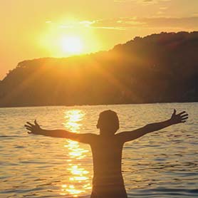 A young child with his arms outstretched on the beach facing the sun