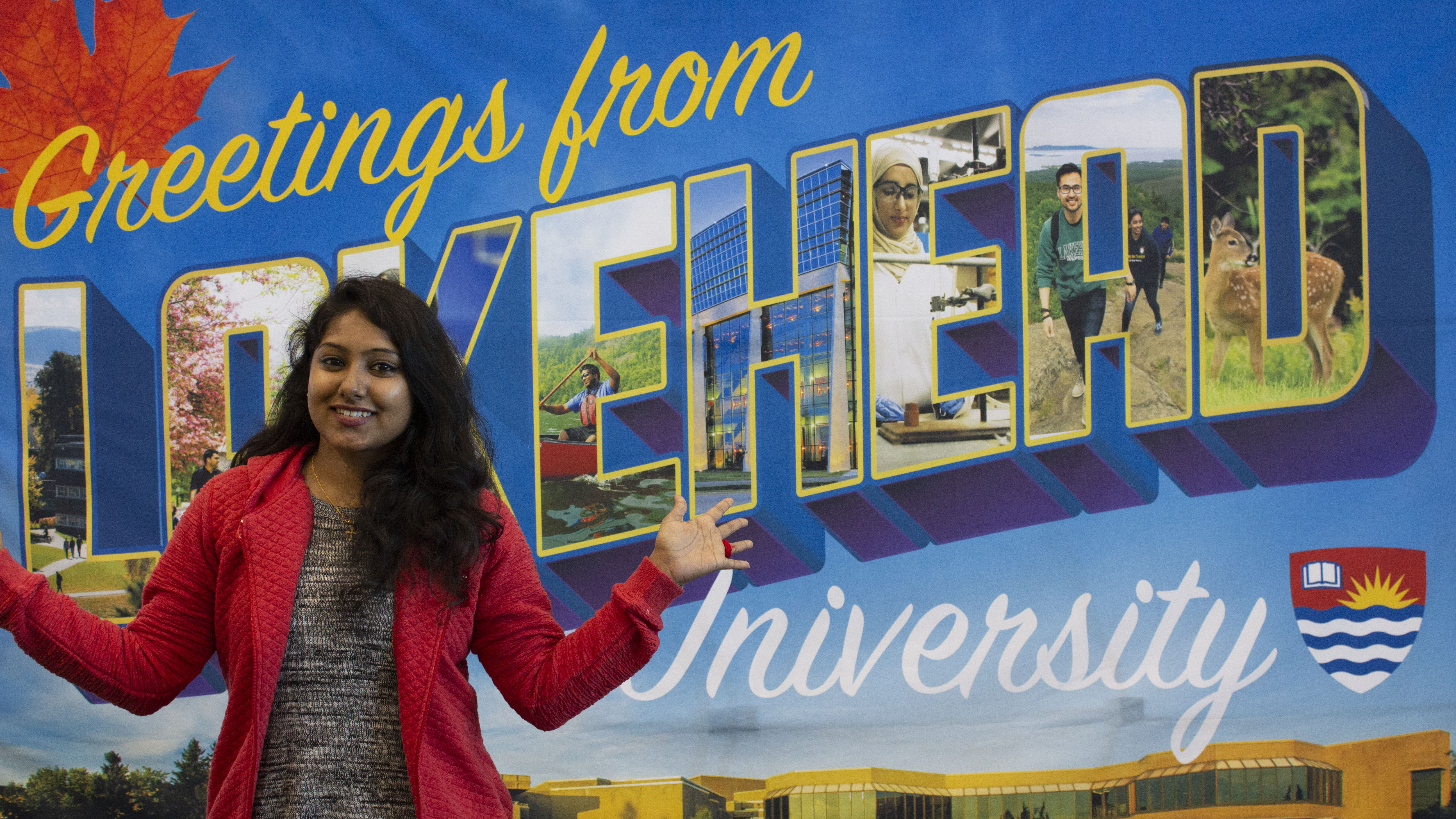 Student in front of a sign that reads "Greetings from Lakehead"