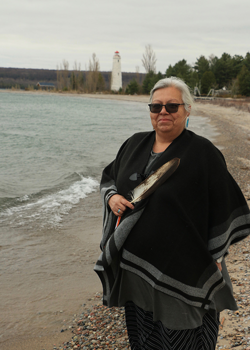 Trish on the sandy shores of a lake holding a ceremonial feather