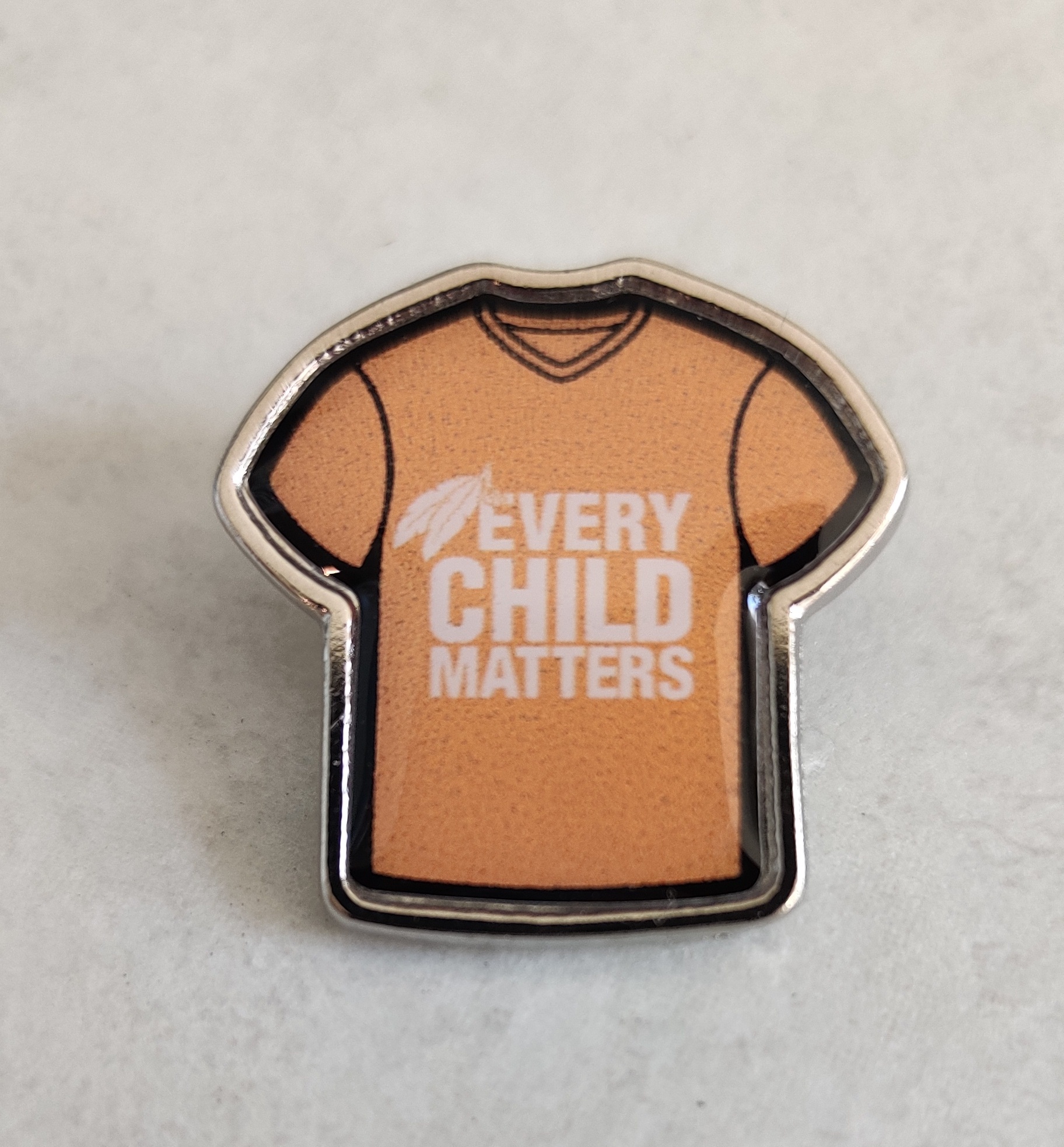 The Every Child Matters pin features the slogan on an orange shirt with eagle feathers beside the E