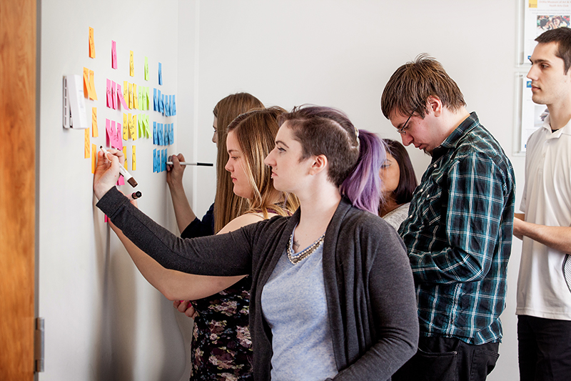 Students filling out sticky notes on a wall