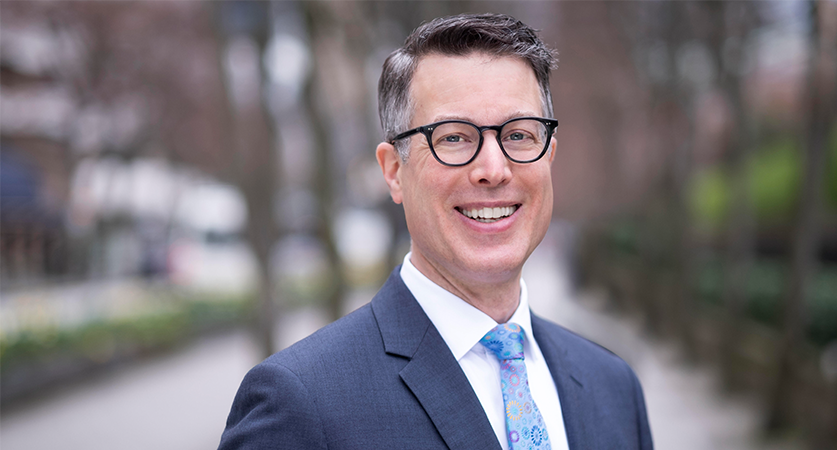 A man wearing black rimmed glasses with short cropped dark hair