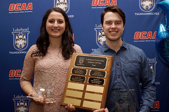 A smiling woman with dark hair and a smiling man with short dark hair hold a wooden plaques stating Athletes of the Year