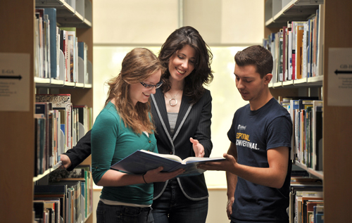 This is a picture of a professor holding a book while helping two students. Click to learn more about our return policy