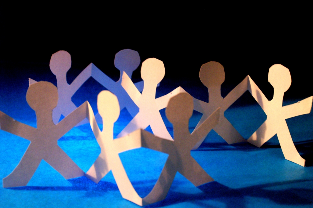Paper cut out humans holding hands in a semi-circle.
