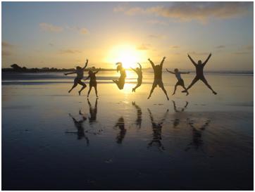 Sevent people jumping in the air on a beach in front of a beautiful sunset