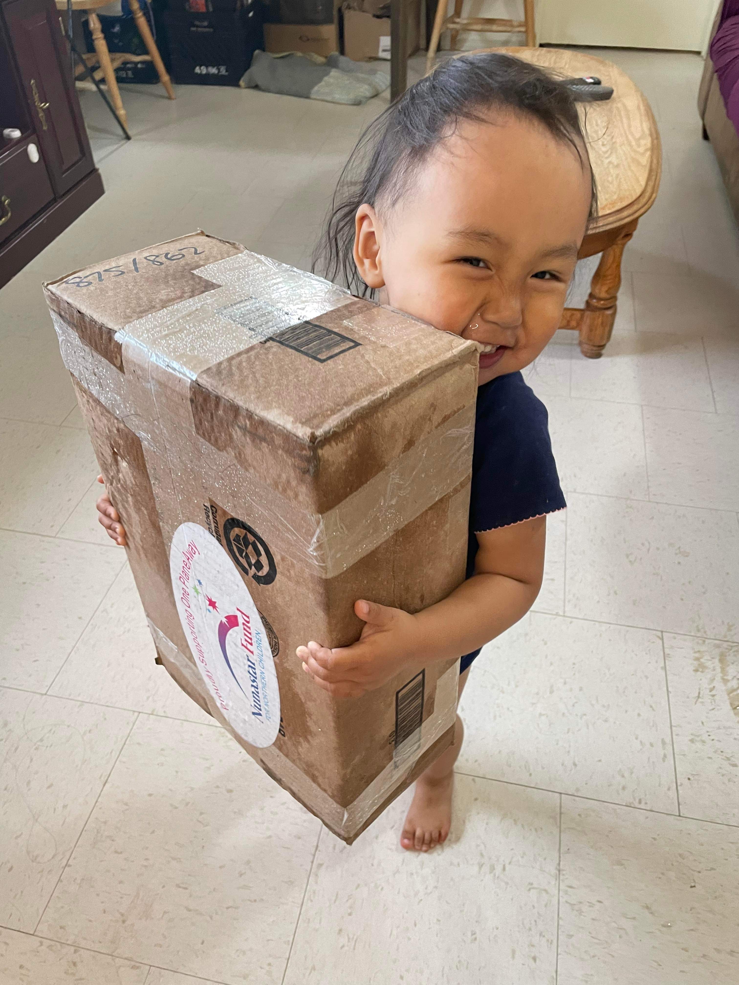Smiling toddler carries a package from One Plane Away