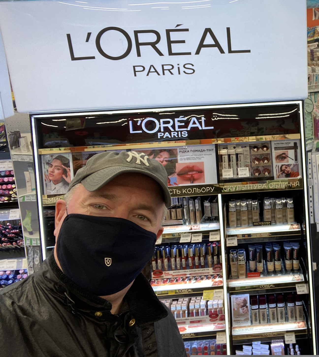 Mark Sawchuk stands in front of a store display of L'Oreal makeup products while wearing a face mask