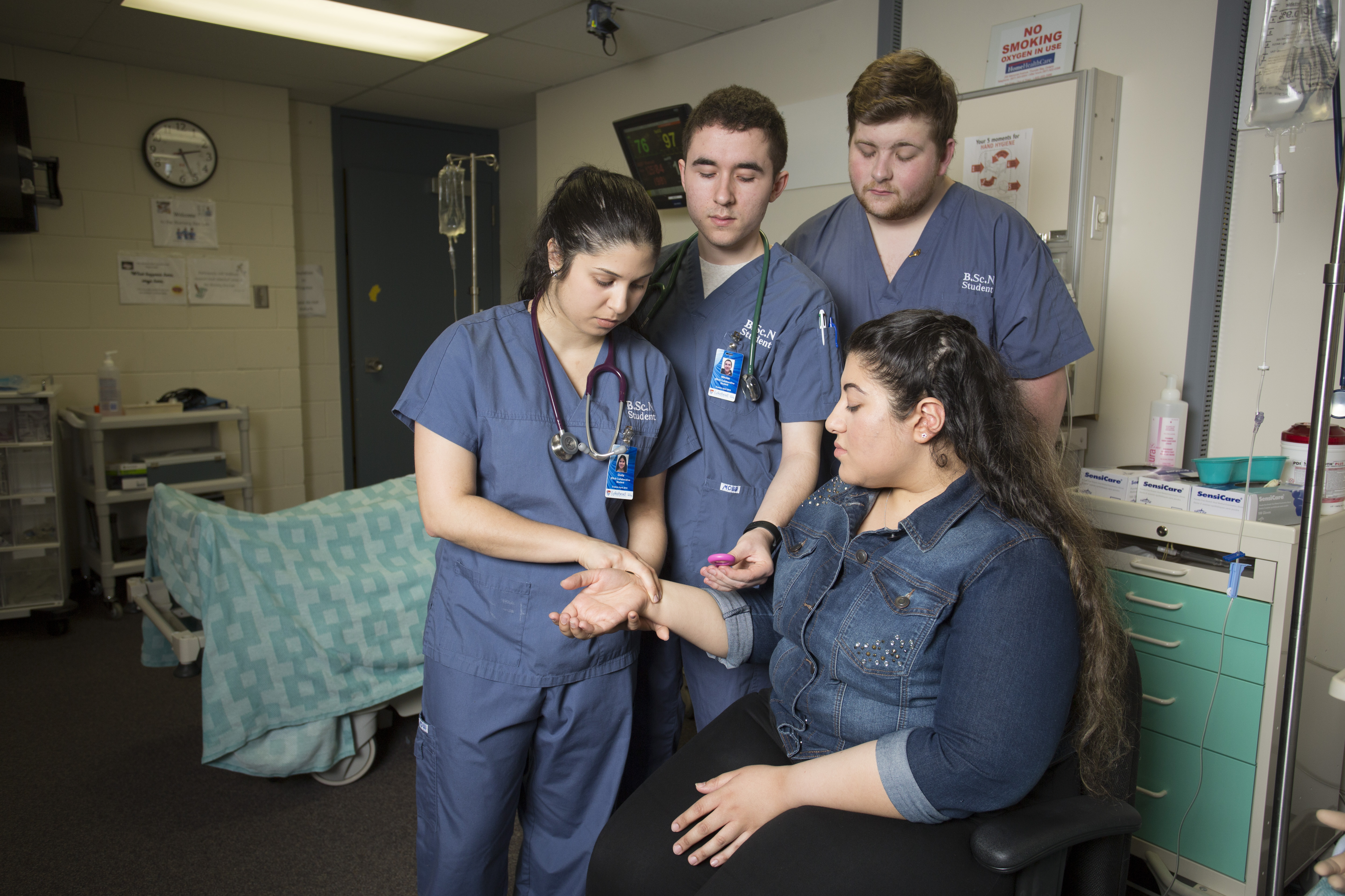 Three nursing students help take a patient's pulse