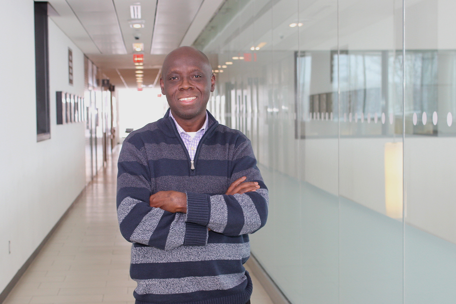 Dr. Olakunle Akingbola stands in a hallway on the Orillia campus with his arms crossed and smiles at the camera