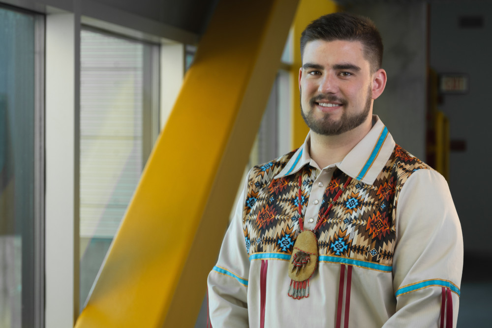 Tristen Brown wears a ceremonial shirt with Indigenous designs and has a beaded pouch with claws around his neck