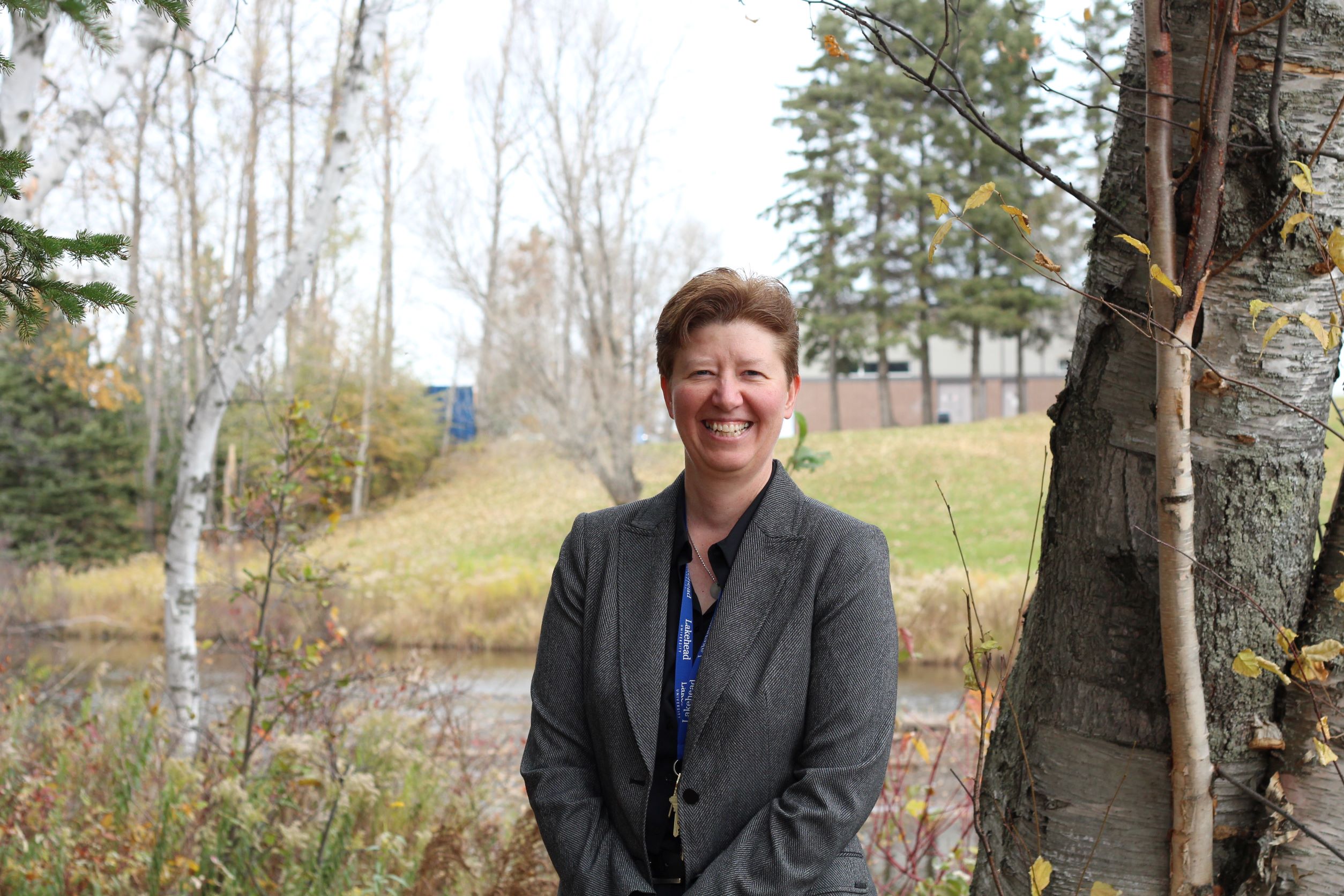 Dr. Vicki Kristman stands outside on the Thunder Bay campus near river and trees