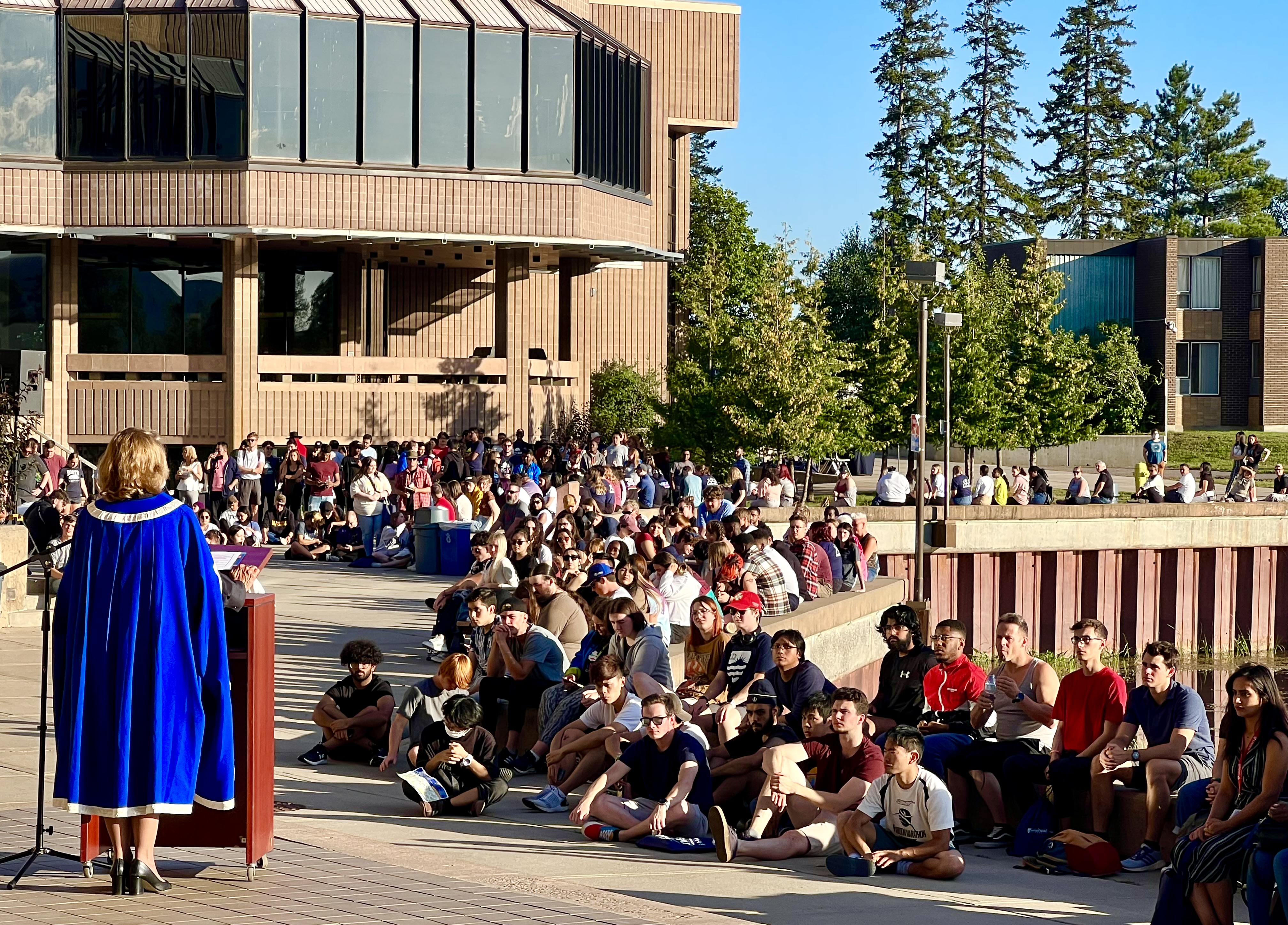 Lakehead President Moira McPherson dressed in formal robes gives a speech to Lakehead students beside Lake Tamblyn