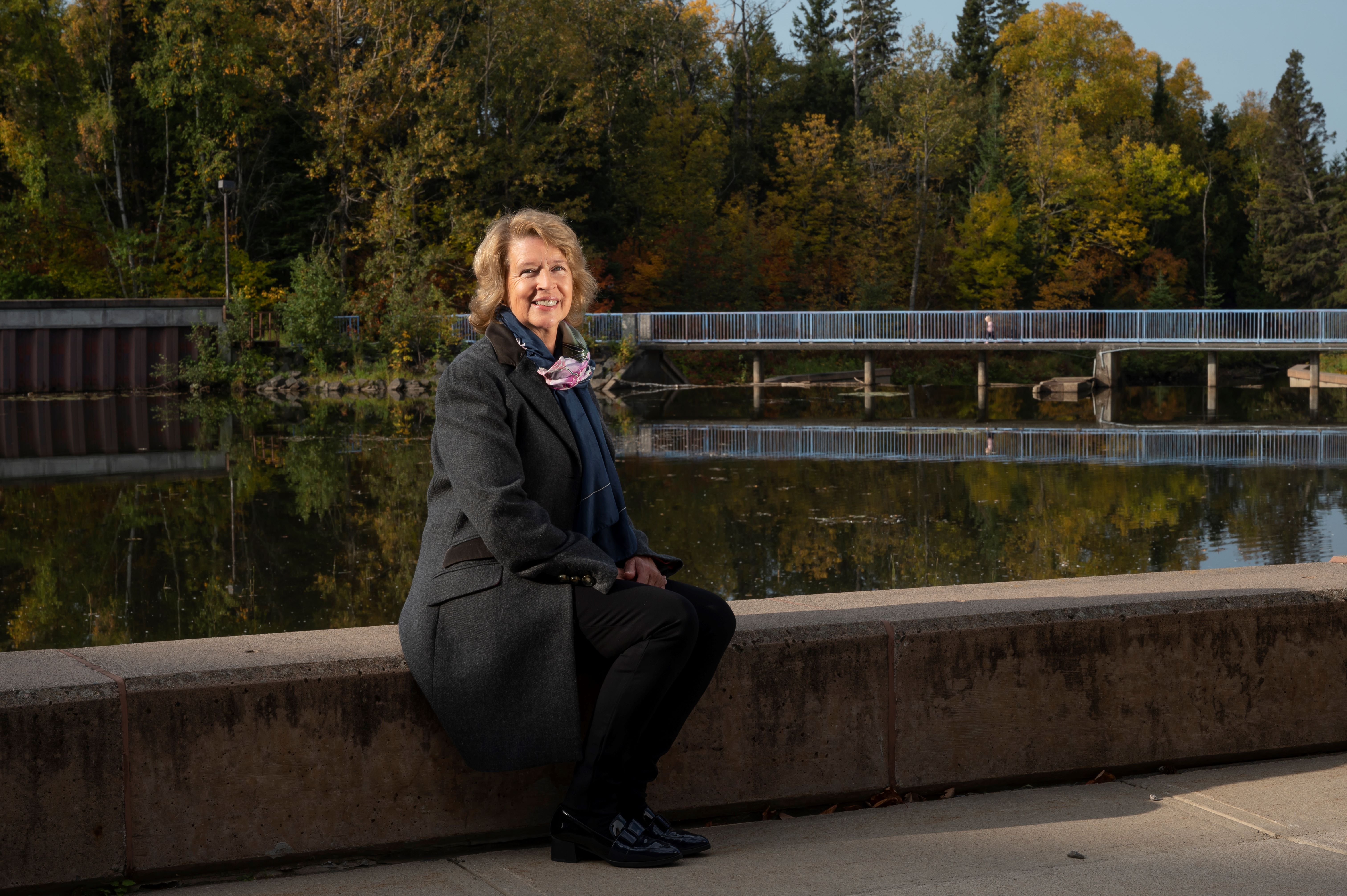 Lakehead University President Moira McPherson sits next to Lake Tamblyn on the Thunder Bay campus on a fall day